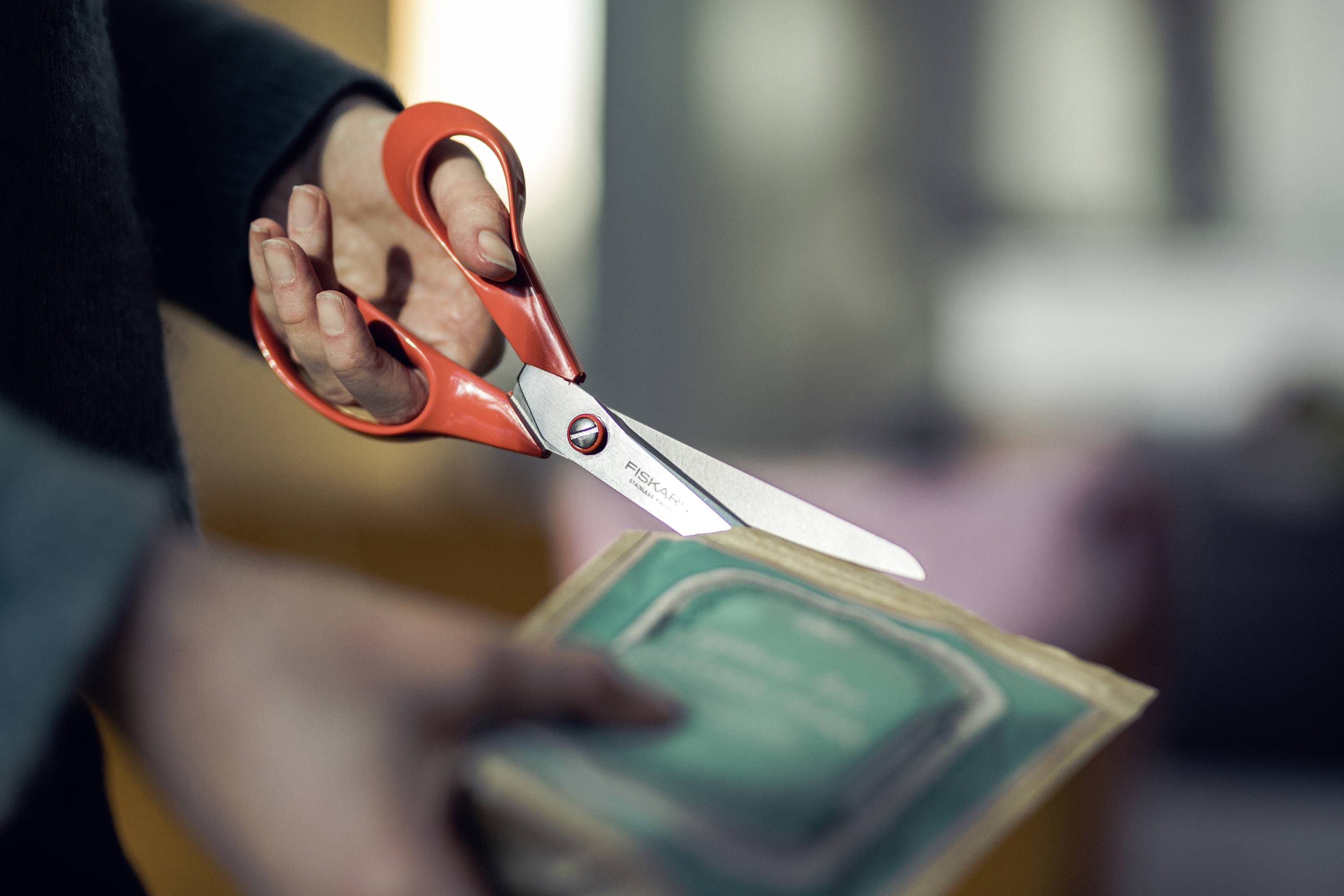 Een persoon knipt een verpakking open met een rood-zwarte schaar. Hij/Zij houdt de schaar in de rechterhand.