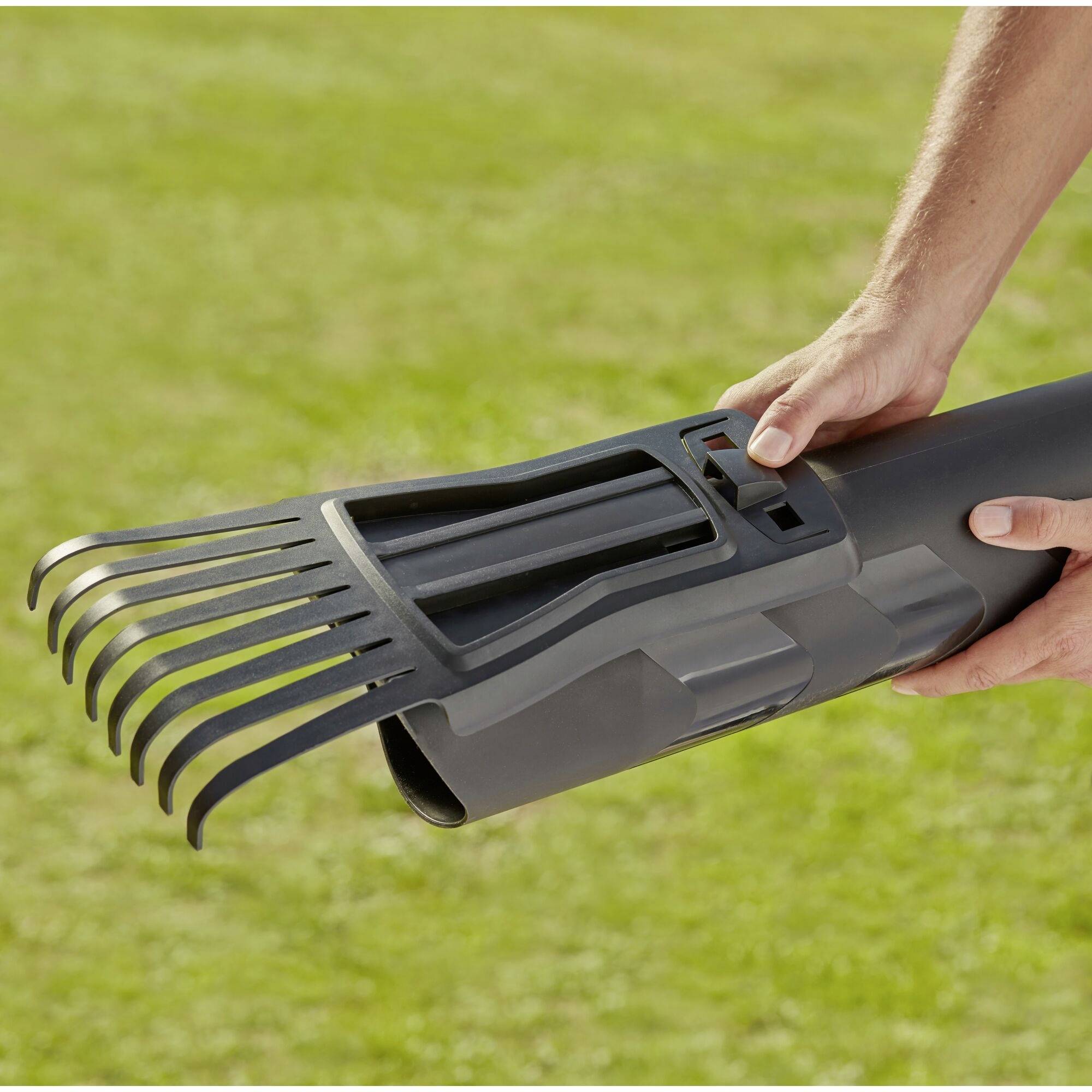 Een persoon houdt een grijs apparaat met zwarte kamtanden vast, dat eruitziet als een telescoopbuis, boven een groene grasvlakte.