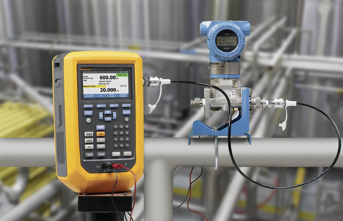 Een gekalibreerd meetinstrument naast een druksensor in een industriële installatie; beide apparaten zijn door kabels verbonden.