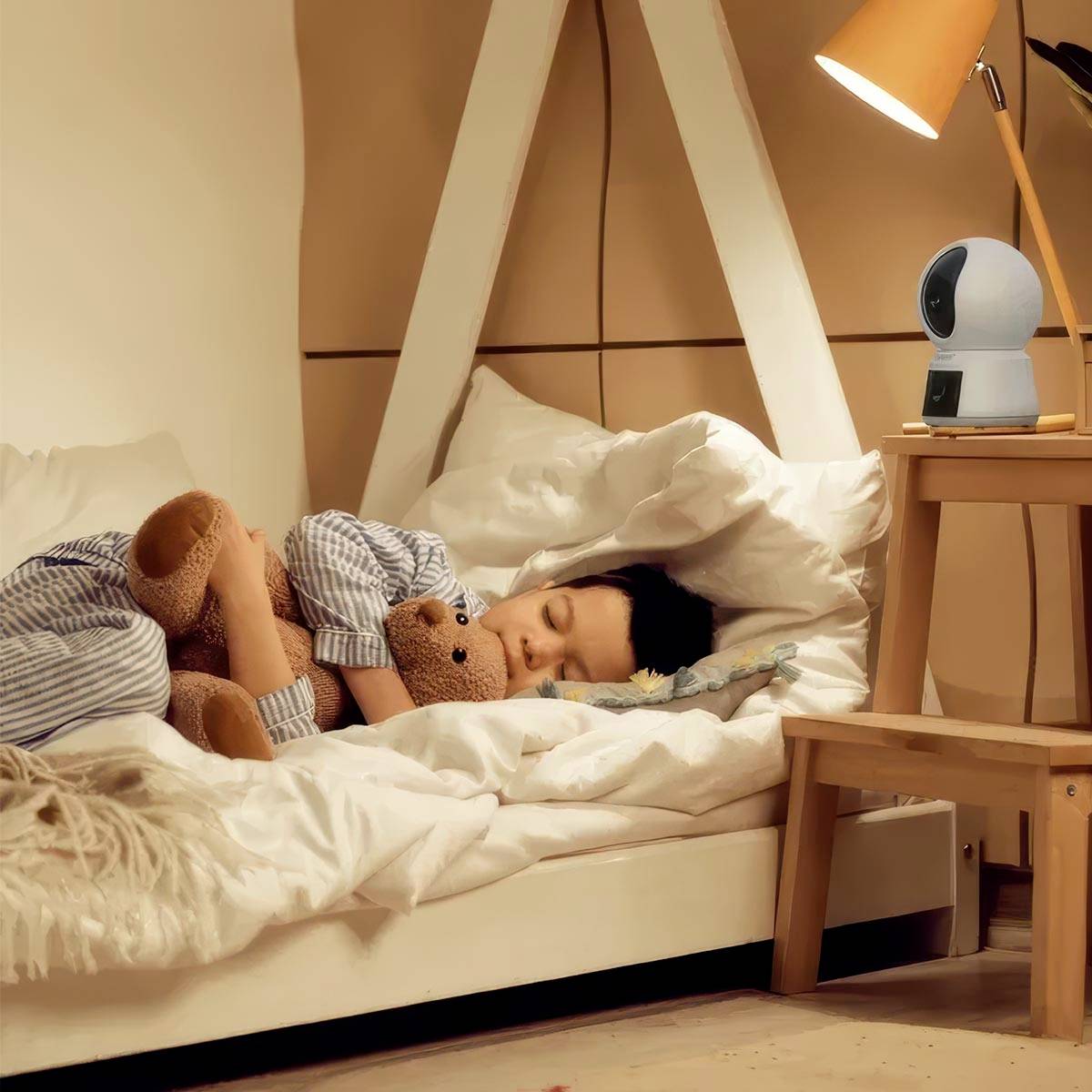 Kleinkind slaapt in bed en houdt een teddybeer stevig vast. Op de achtergrond schijnt een lamp naast een babyfoon op een tafel.
