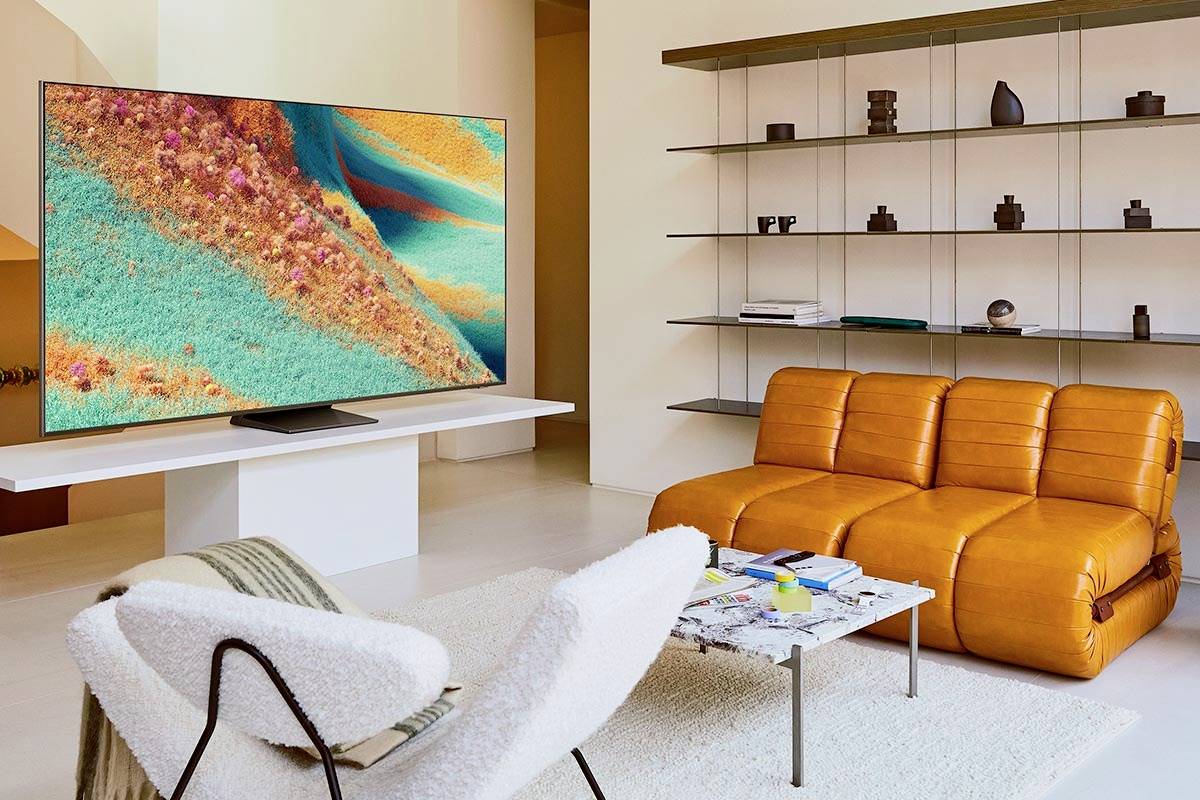 Woonkamer met een grote televisie die kleurrijke landschappen vertoont, een modern bank, fauteuil en een tafel ervoor. Boekenkasten op de achtergrond.