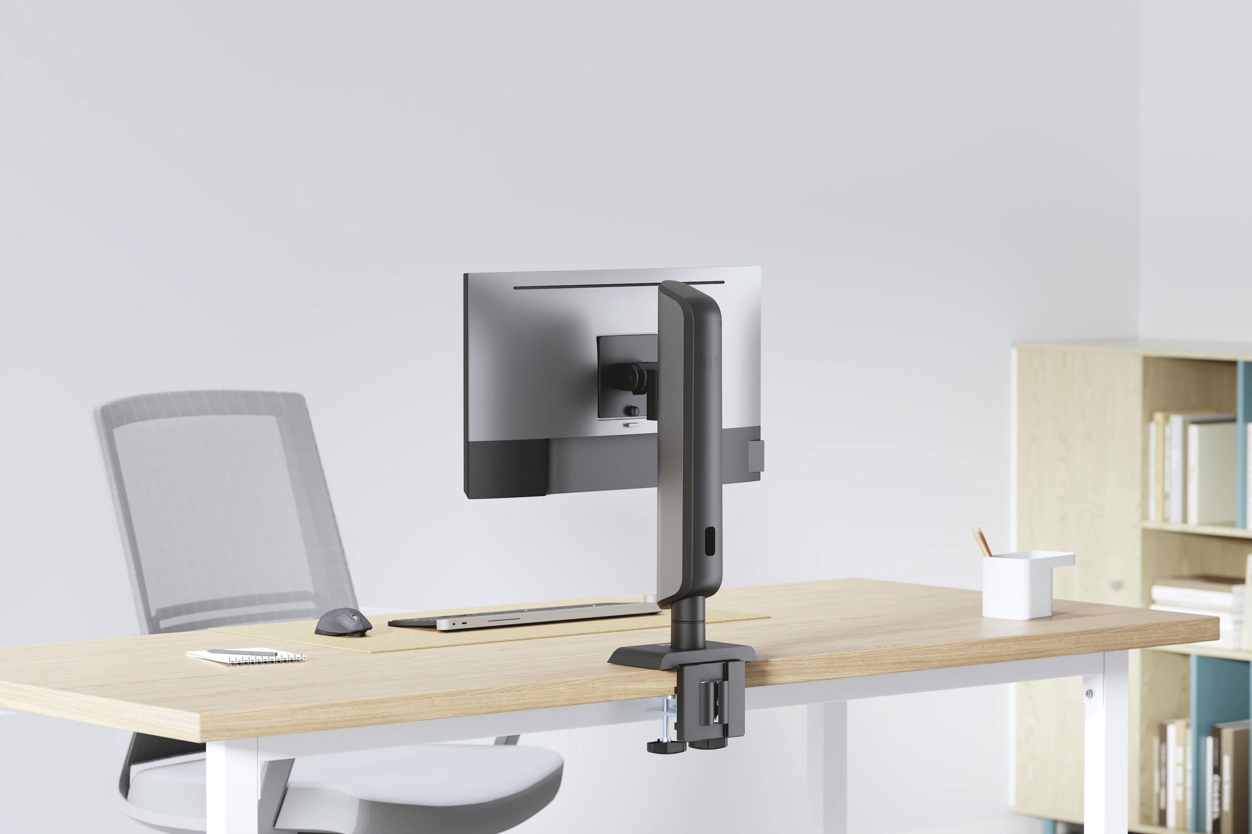 Een moderne kantoorwerkplek heeft een bureau met een computermonitor gemonteerd op een verstelbare arm, een toetsenbord, een muis en een kopje op het oppervlak.