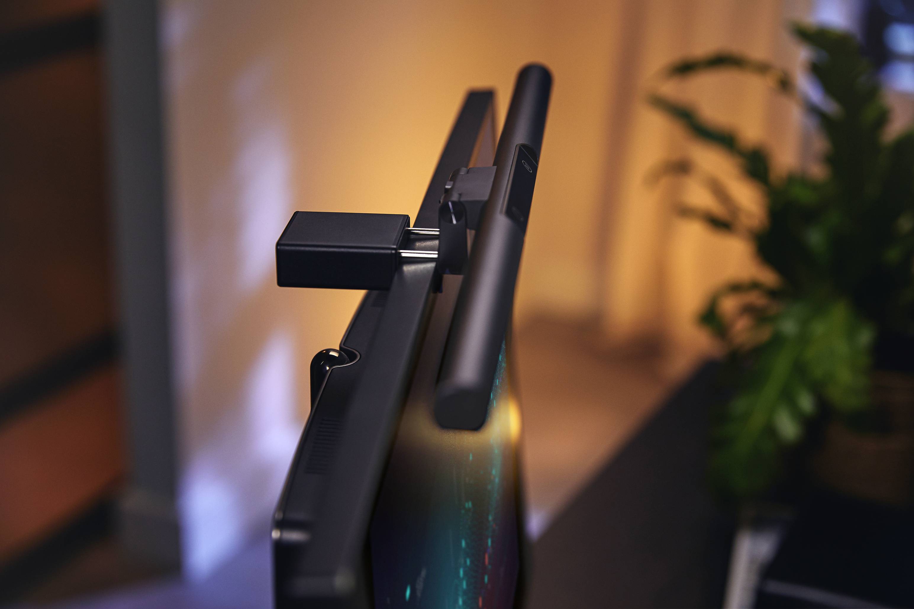 Een monitorlamp is gemonteerd op een flatscreen, met een onscherpe plant op de achtergrond. Verlicht en modern.