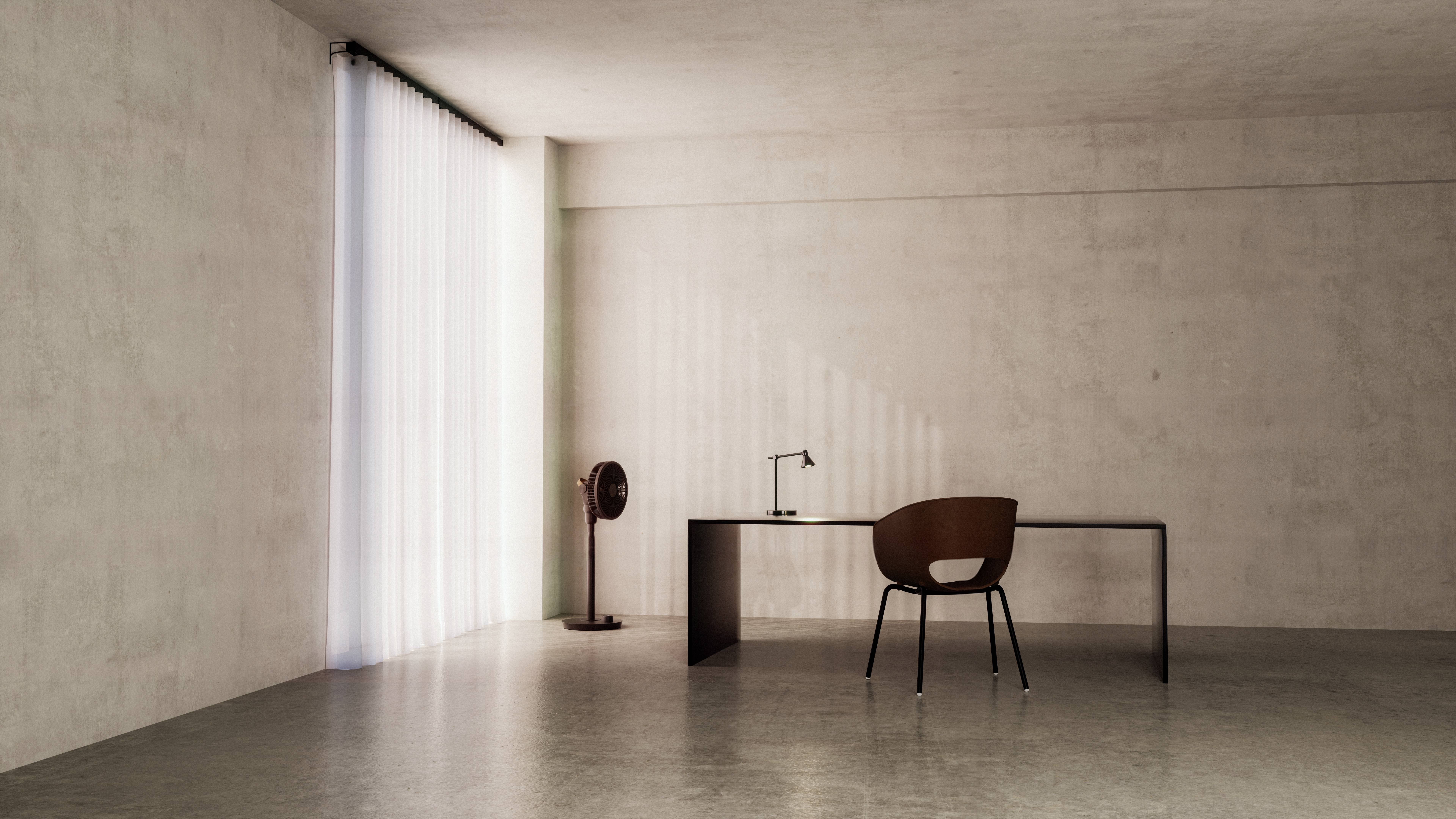 Een minimalistisch ingericht kantoor met een donkere, eenvoudige tafel en een stoel. Licht stroomt door een hoog gordijn aan de linkerkant.