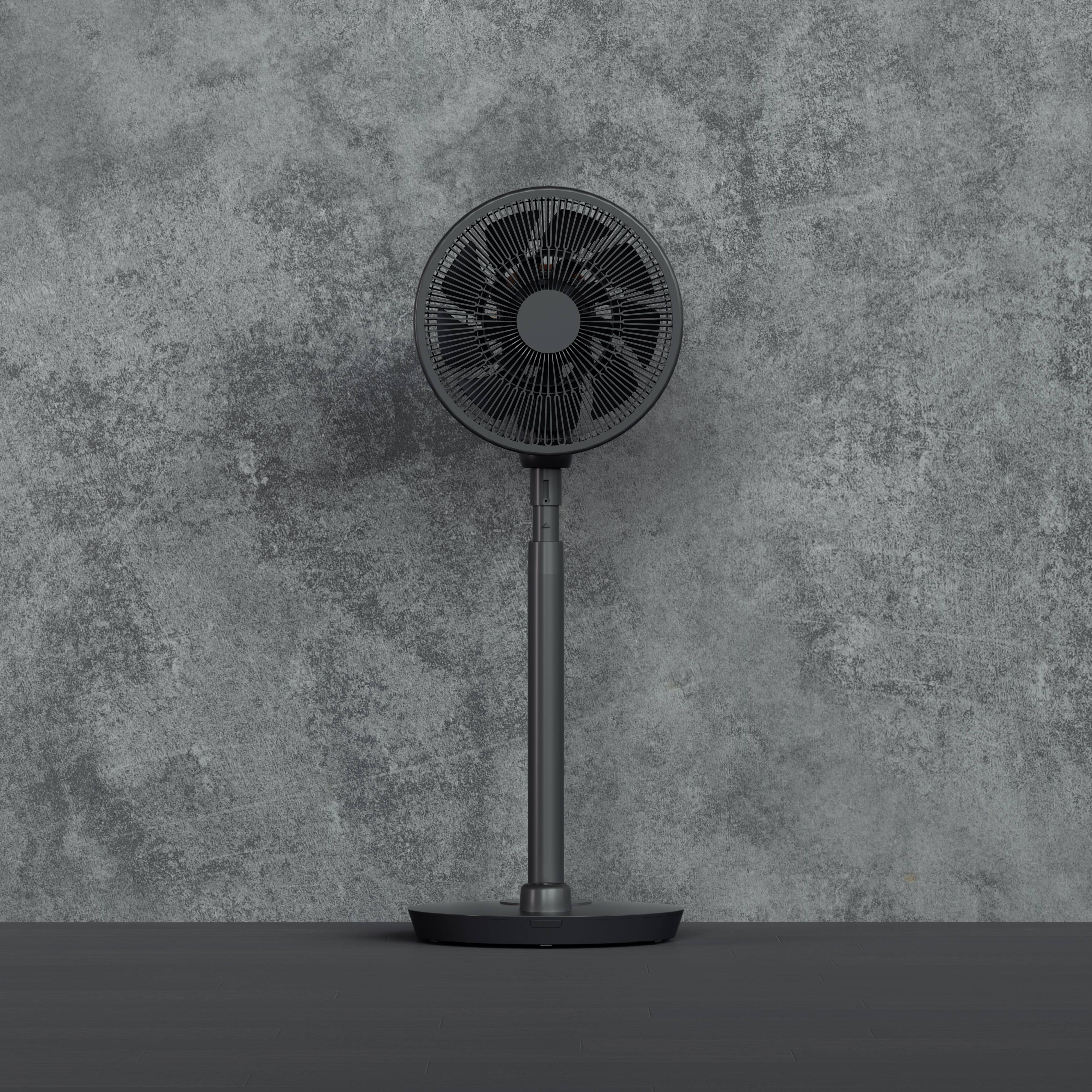 Een staande ventilator voor een grijze betonnen muur. De ventilator is zwart en heeft een ronde roosterkop.