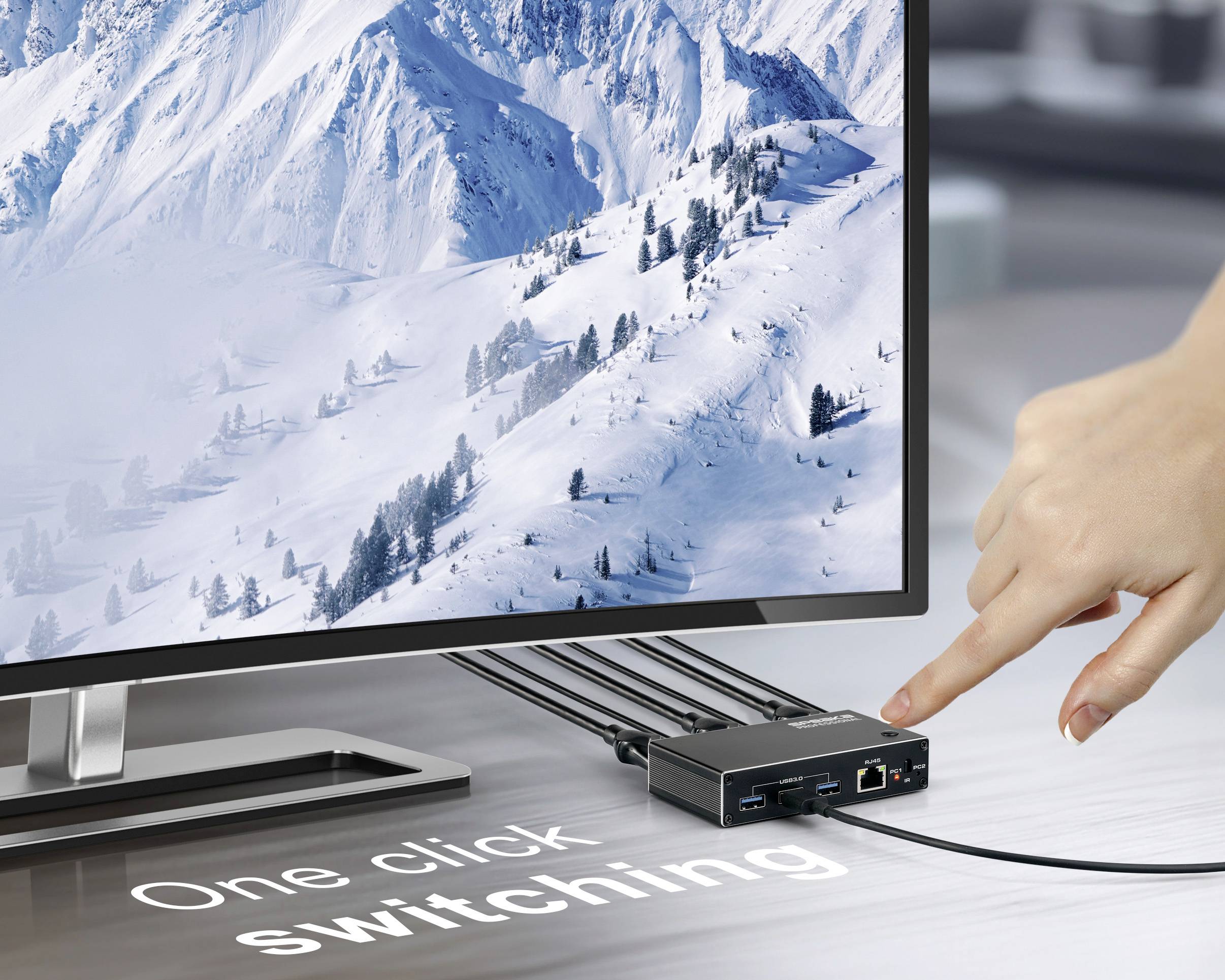 Een hand drukt op een knop op een apparaat met het label 'Eén klik omschakelen', verbonden met een monitor waarop een besneeuwd berglandschap wordt weergegeven.