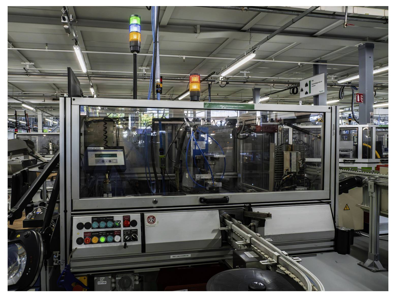 Geautomatiseerde industriële machine op een fabrieksvloer, omgeven door veiligheidsglas met statusindicatoren en bedieningsknoppen, die materialen op een transportband verwerkt.