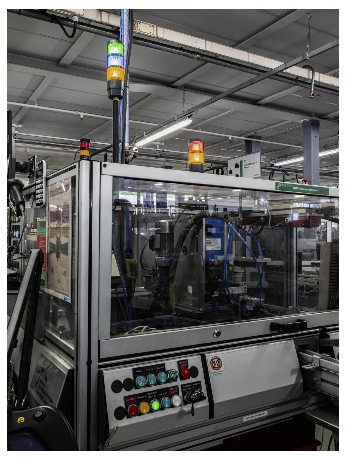 Geautomatiseerde industriële machine op een fabriekslijn met flitsende groene, gele en rode statuslampjes en bedieningsknoppen op de voorgrond.