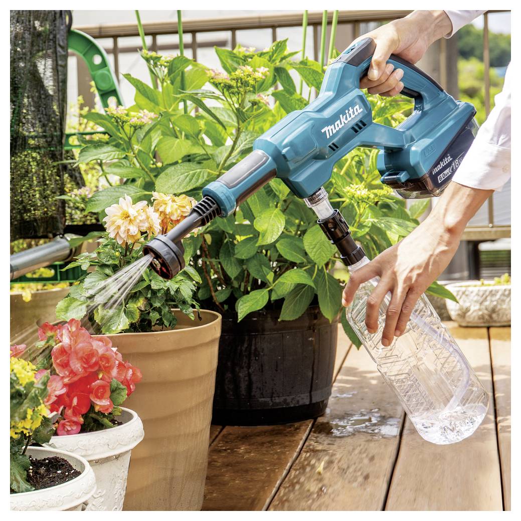 Een persoon gebruikt een blauwe Makita handapparaat om potplanten water te geven op een houten terras, met verschillende planten op de achtergrond.