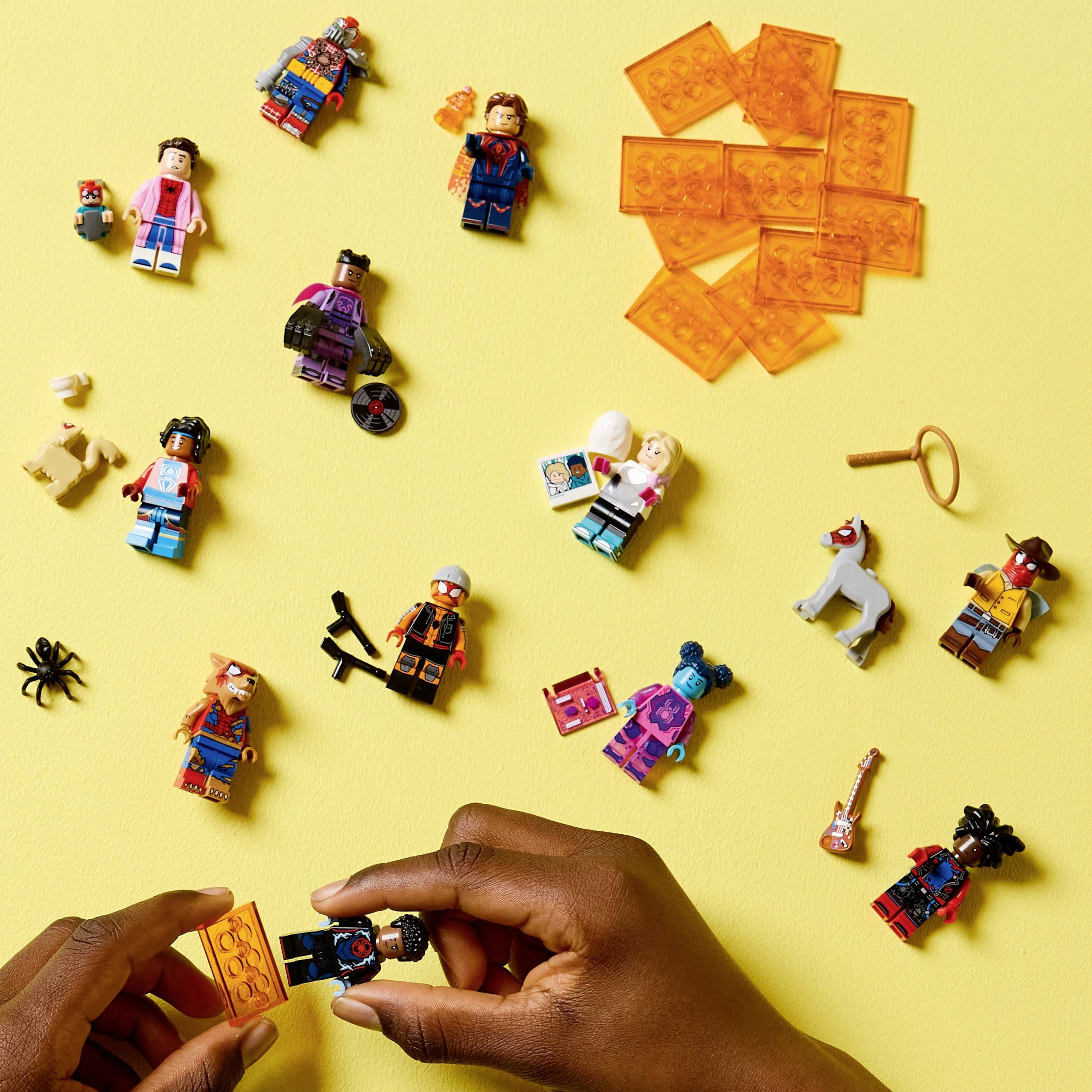 Handen die een LEGO-figuurtje in elkaar zetten, omringd door verschillende gedemonteerde LEGO-minifiguren en accessoires op een gele achtergrond.