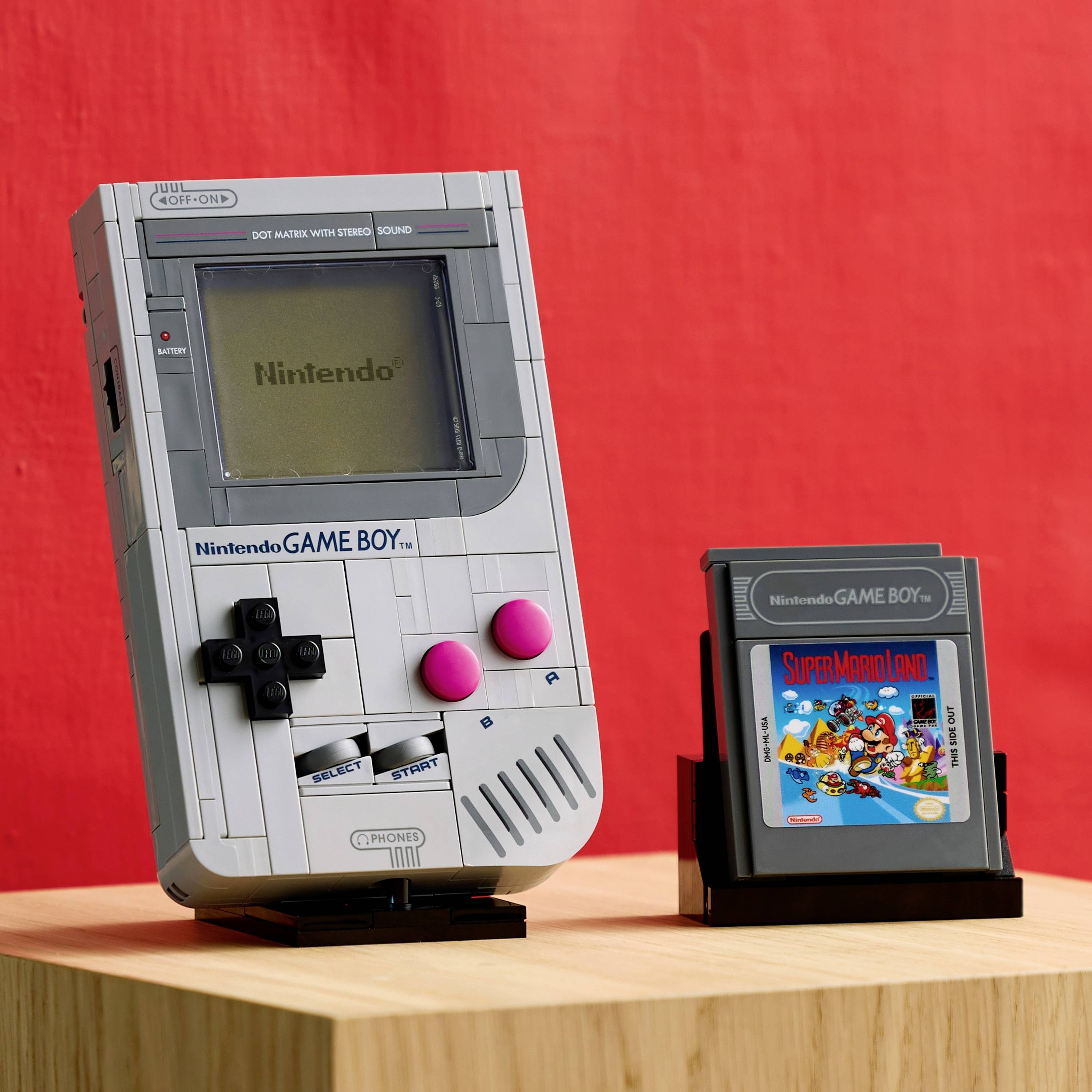 Een vintage Nintendo Game Boy met een 'Super Mario Land' cartridge op een houten oppervlak. De Game Boy heeft roze knoppen en een grijze behuizing.