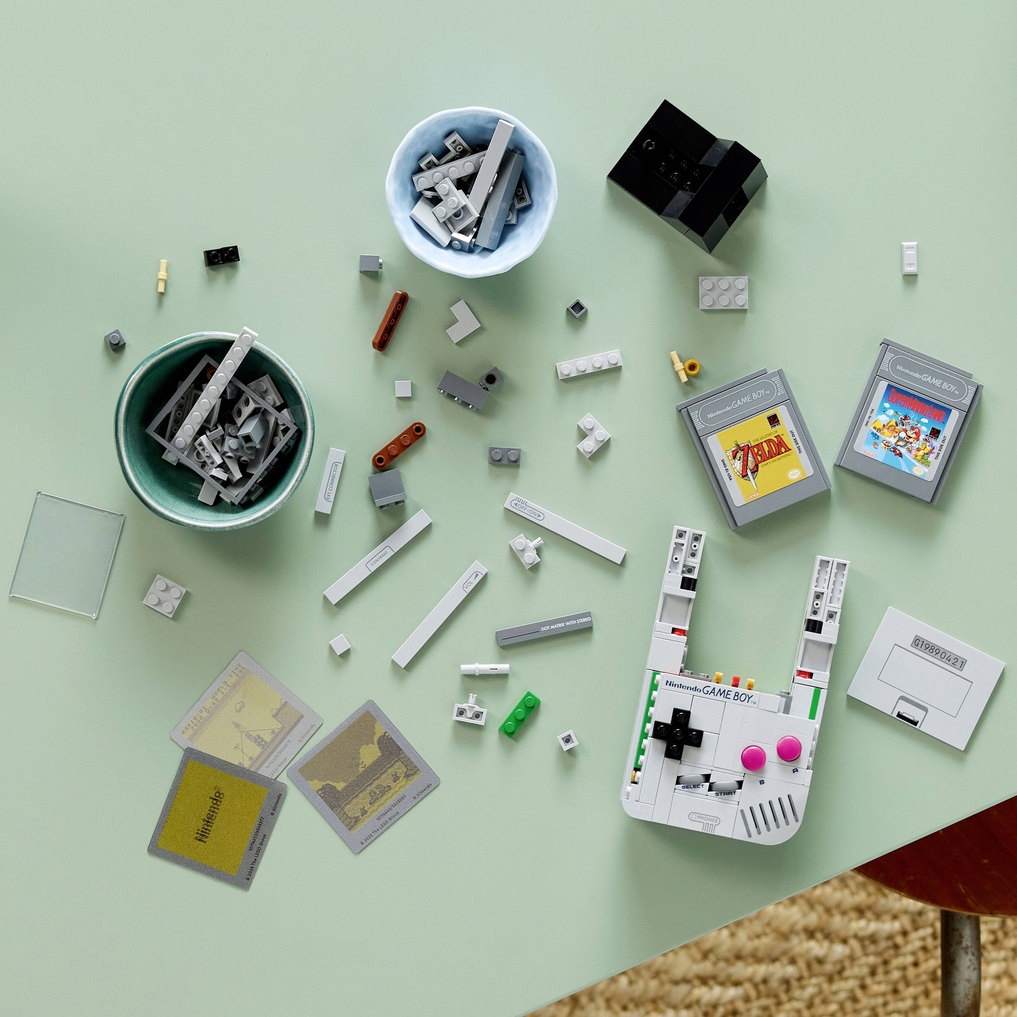 Legoblokjes verspreid over een oppervlak, inclusief kleine schaaltjes met blokken, een mini retro gameconsole, gameCartridges en apparaatonderdelen.