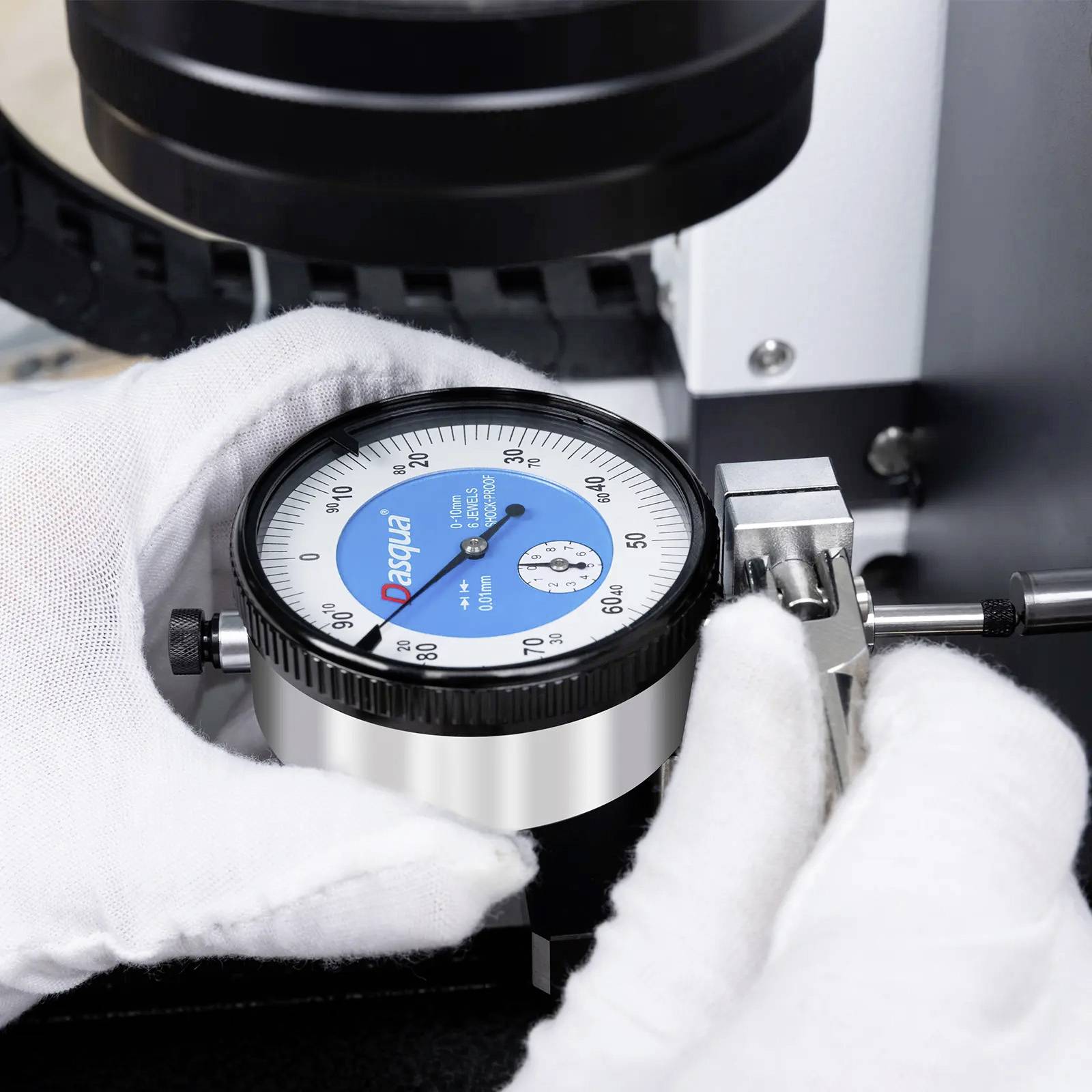 Een persoon stelt een blauwe en witte meetklok met gehandschoende handen af, waarbij de precisie van een machinedeel wordt gemeten. De meetklok geeft '0,02 mm' aan.