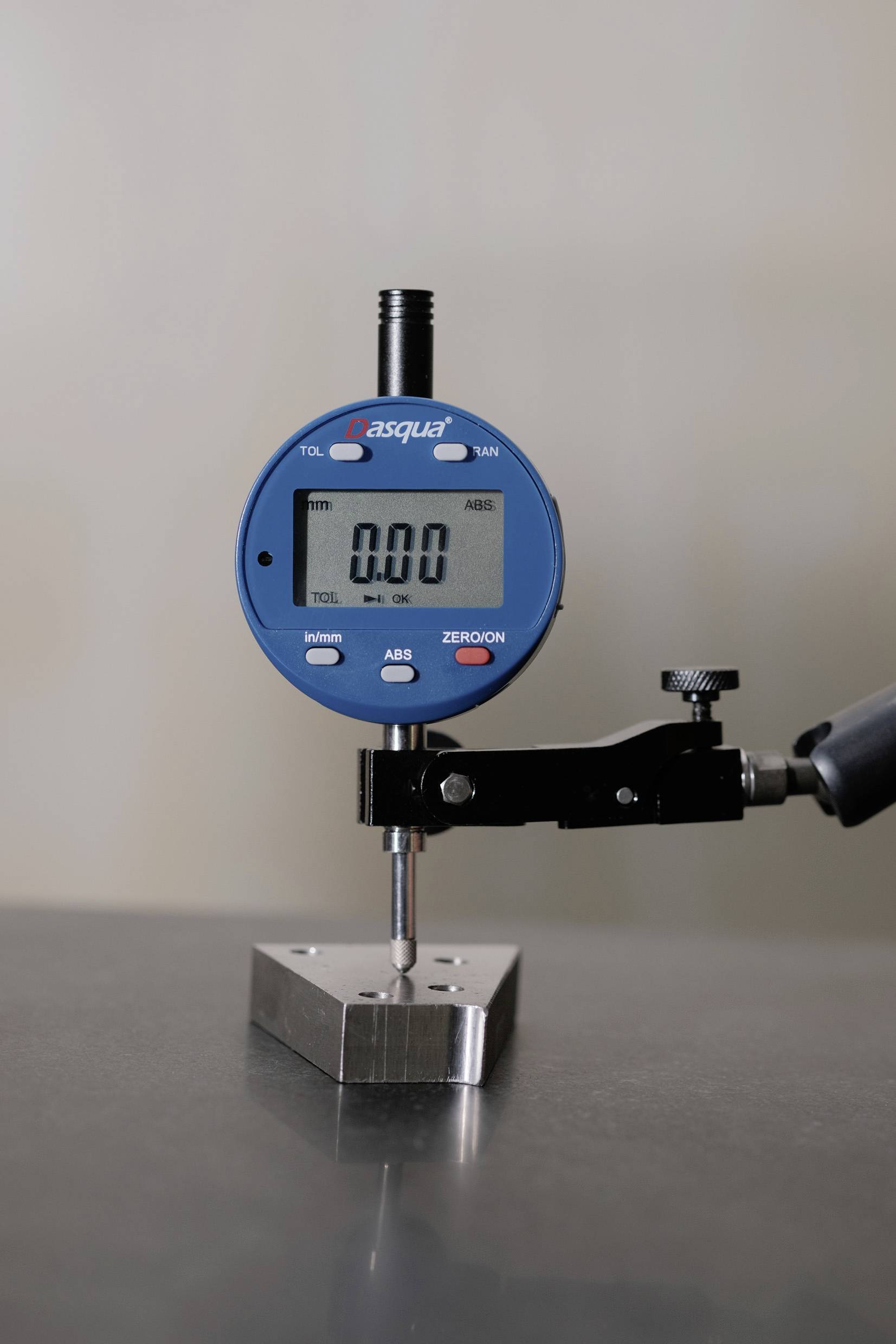 Digitale schuifmaat die een klein metalen blok op een vlak oppervlak meet, met '0.00' op het scherm weergegeven, wat aangeeft dat geen afwijking wordt gedetecteerd.