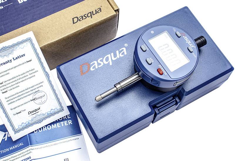 Een digitale durometer met een blauwe behuizing met het 'Dasqua' logo, naast gebruiksaanwijzingen en een garantiebrief, wat wijst op kalibratie-instrumenten.