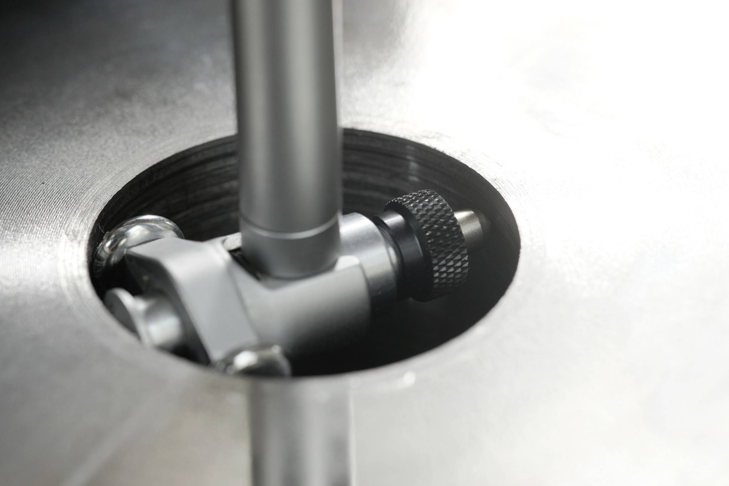 Een close-up afbeelding van een metalen onderdeel met een cilindrische steel en een gegroefde knop, waarschijnlijk deel van een machine of apparatuur.