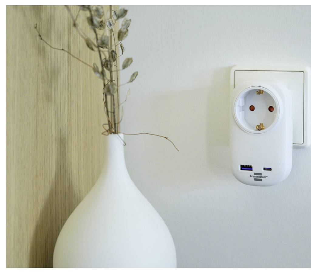 Witte vaas met gedroogde stengels naast een wandcontactdoos en insteekapparaat op een effen wand.