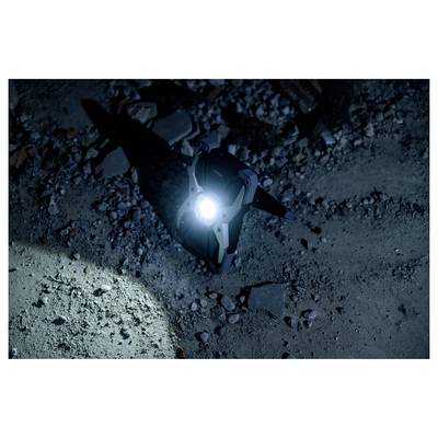 Een klein apparaat met een helder licht schijnt op rotsachtige grond in het donker.