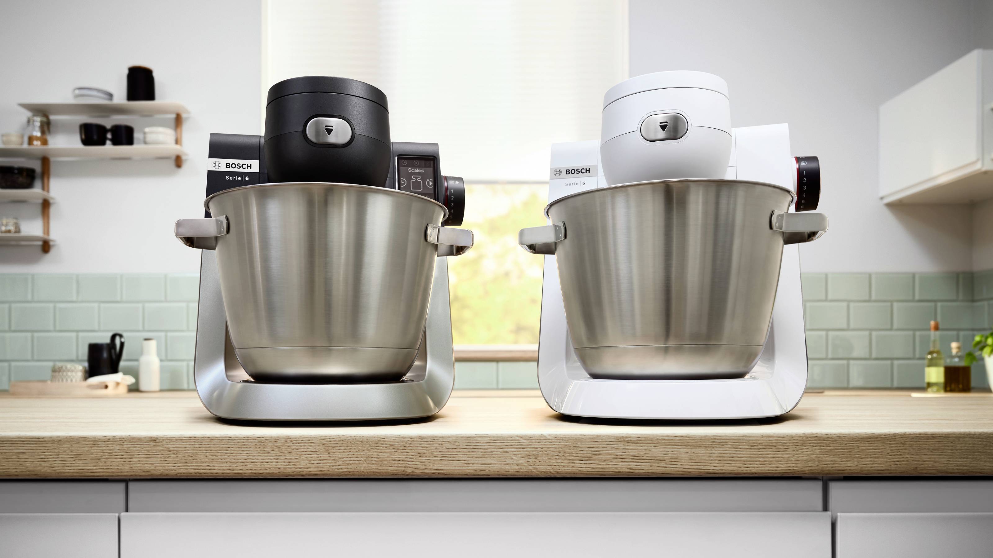 Twee standmixers op een aanrecht, één zwart en één wit, met roestvrijstalen kommen, tegen een licht overgoten keukendecor.