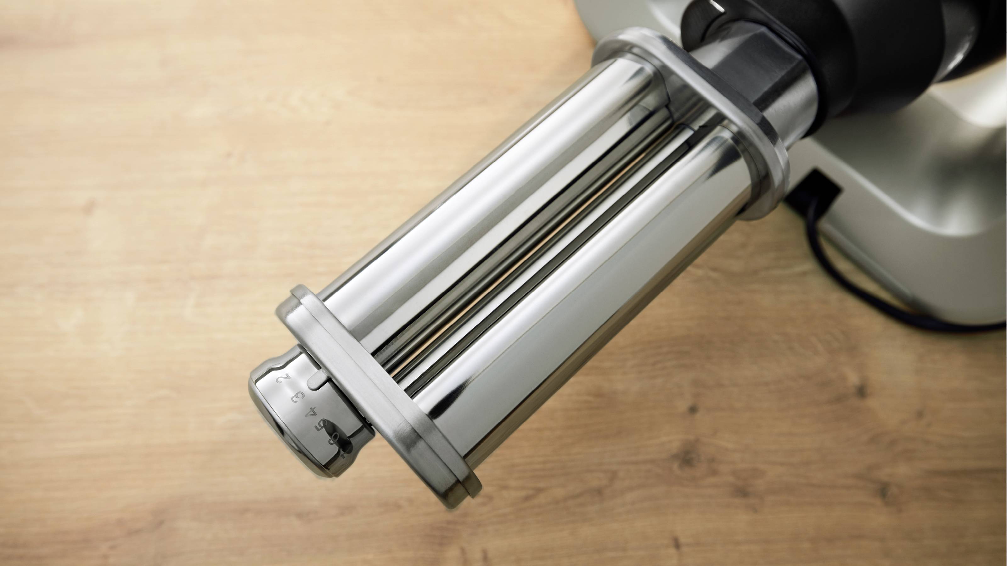 Een pastamachine met een glanzende metalen roller staat op een houten ondergrond, klaar voor gebruik om huisgemaakte pasta te bereiden.
