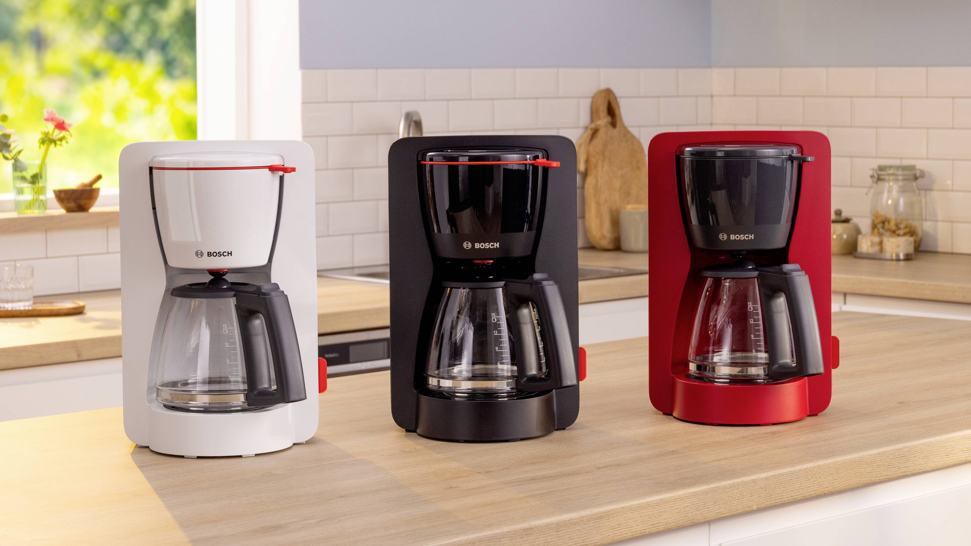 Drie Bosch koffiezetapparaten op een keukentoonbank in wit, zwart en rood. Op de achtergrond een lichte keuken met zonlicht.