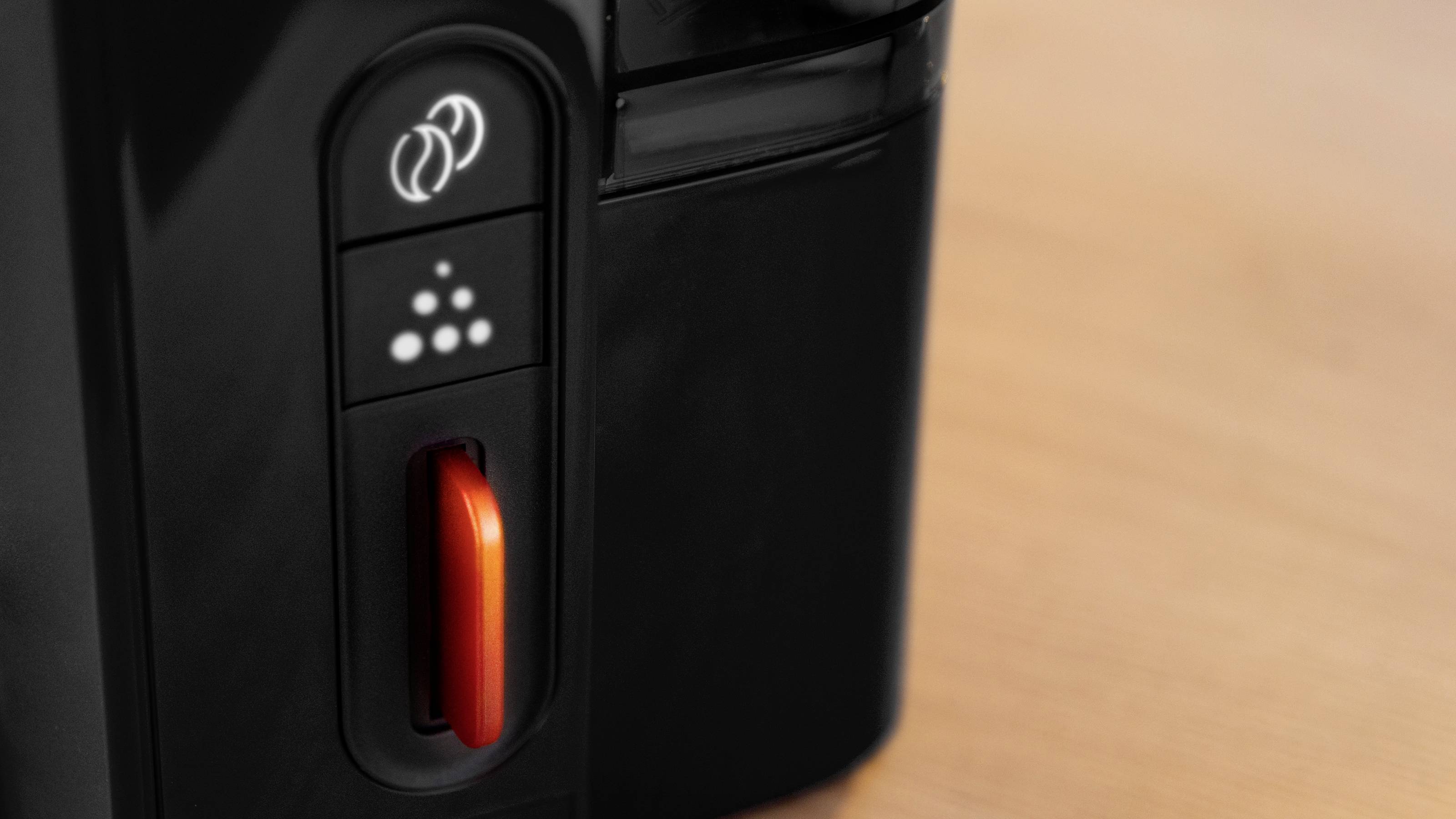 Een close-up van een koffiemachine met een rode hendel en knoppen die instellingen aangeven, geplaatst op een lichthouten oppervlak.