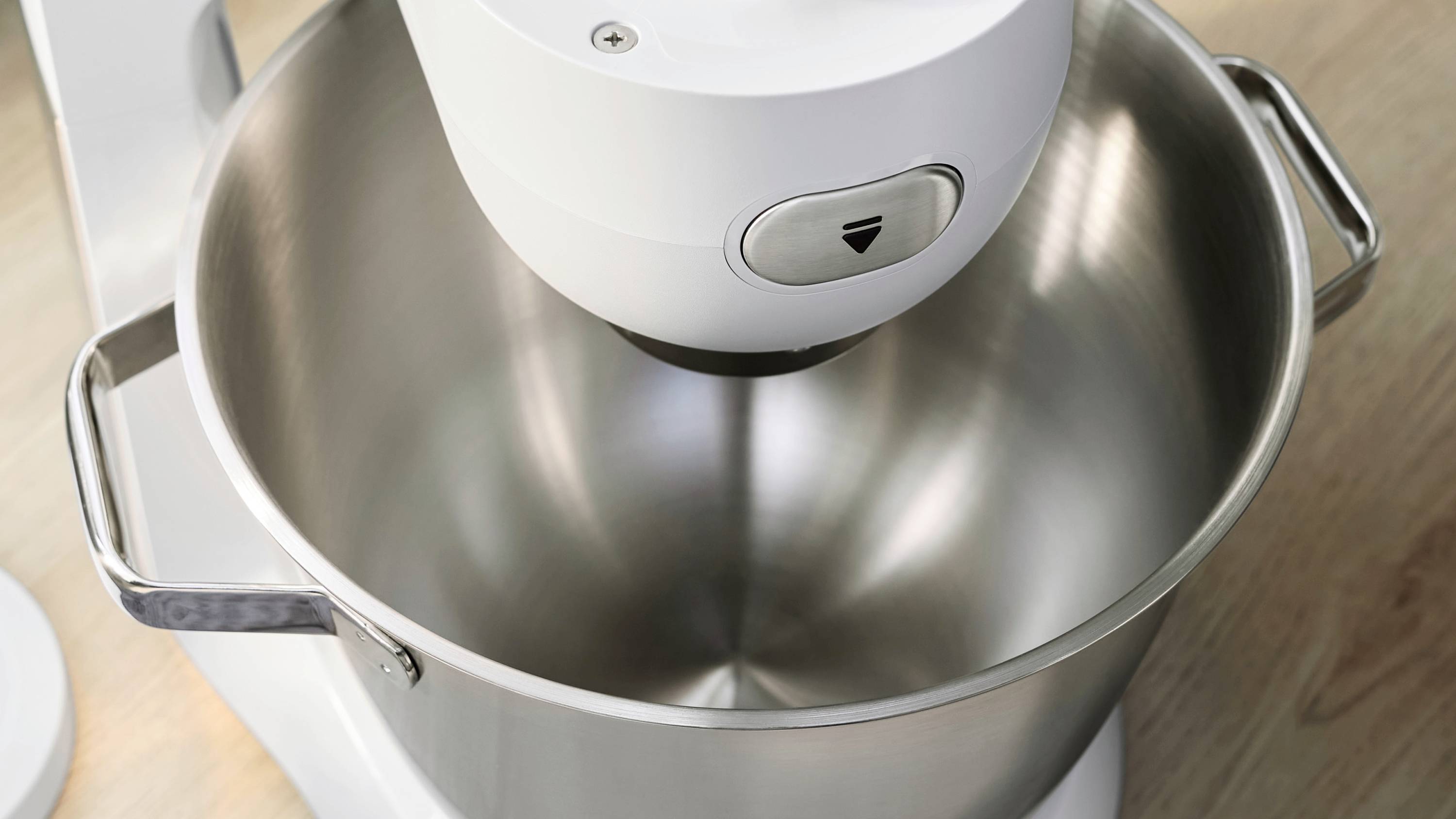 Een kom van roestvrij staal is bevestigd aan een witte mengmachine op een houten aanrecht, klaar om ingrediënten te mengen.