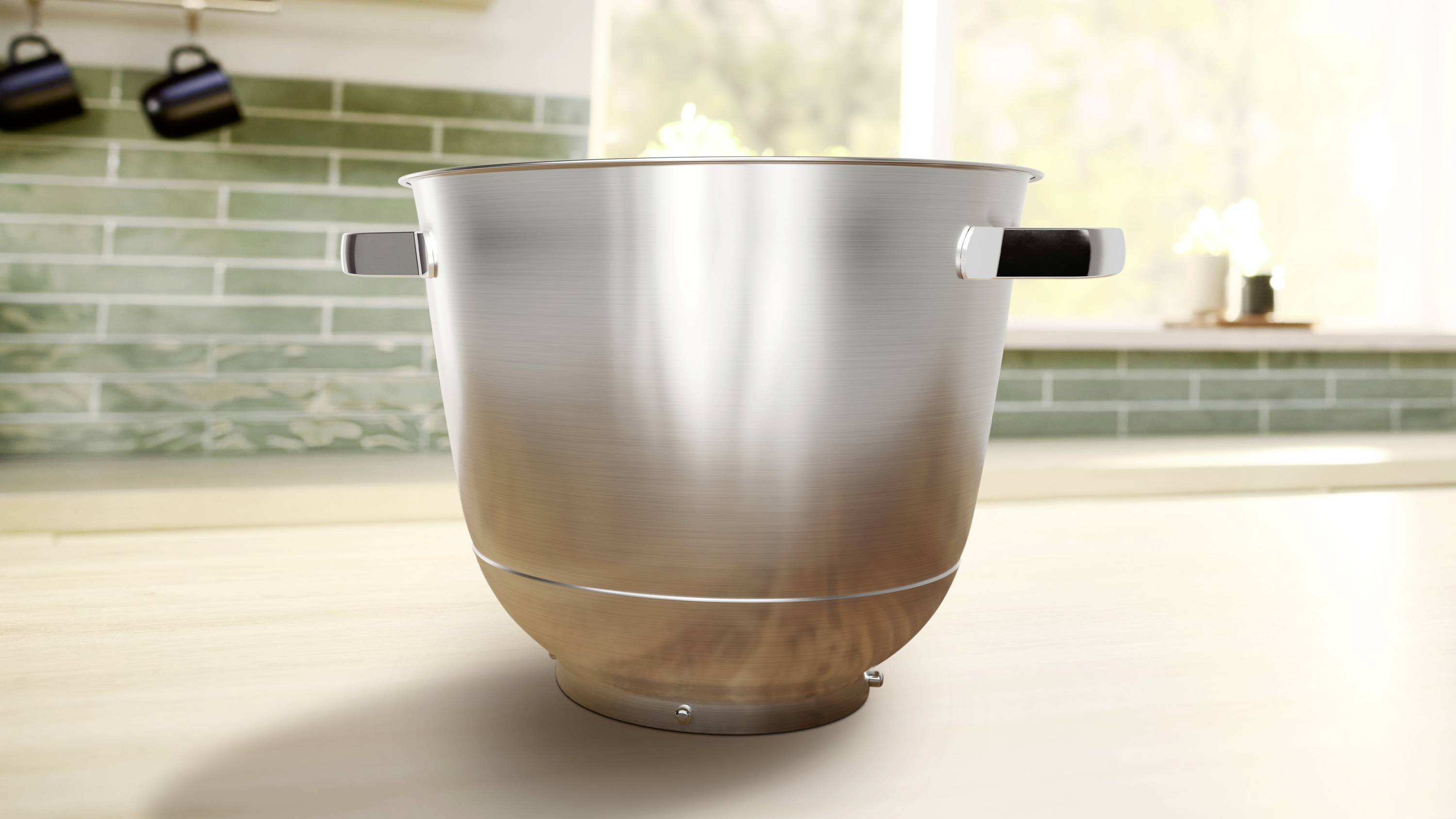 Een grote roestvrijstalen kom met handvatten, geplaatst op een aanrecht met een groene tegelige achterwand en een helder raam op de achtergrond.