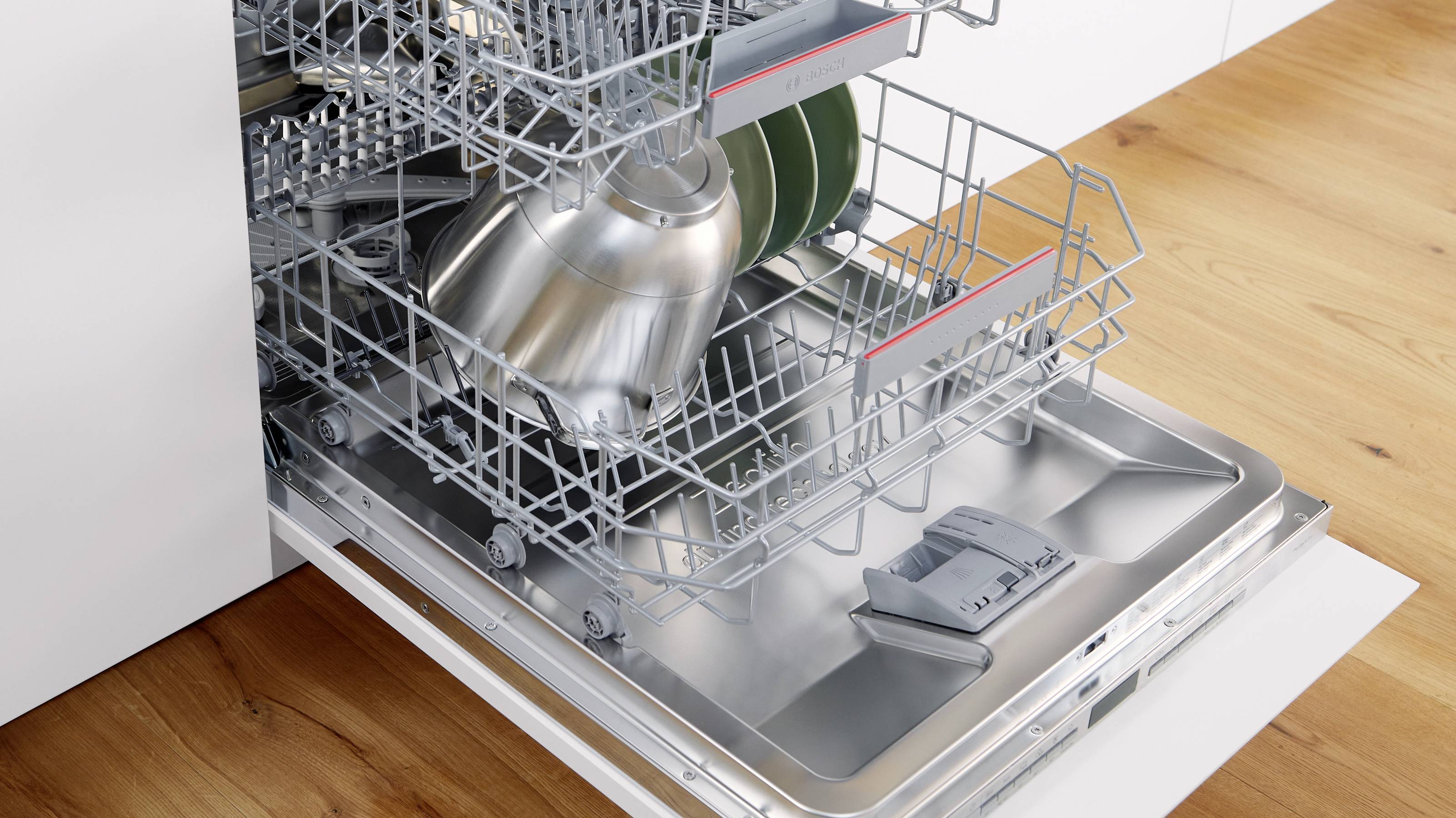 Een open vaatwasser met twee rekken, waarop schone vaat en bestek zijn gerangschikt, met enkele borden en een metalen pan zichtbaar.