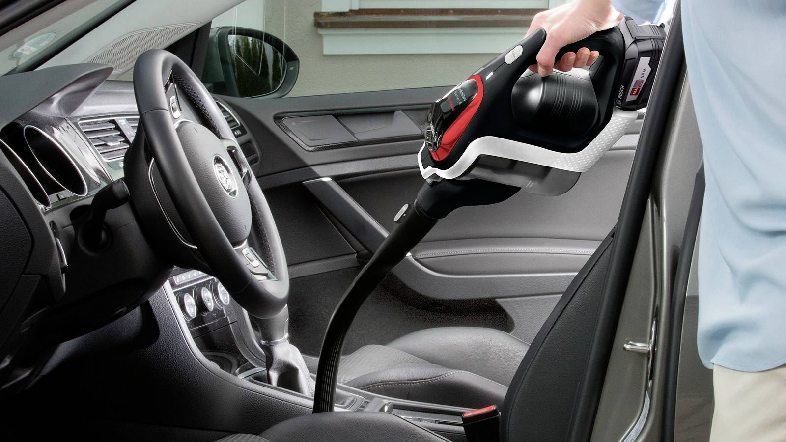 Een persoon die het interieur van een auto stofzuigt met een handstofzuiger, met de focus op de voorste passagiersstoel en het middenconsolegebied.