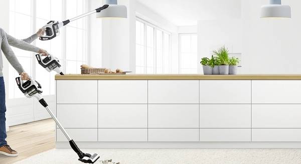 Een persoon demonstreert een veelzijdige stofzuiger met een flexibele steel in een moderne keuken.