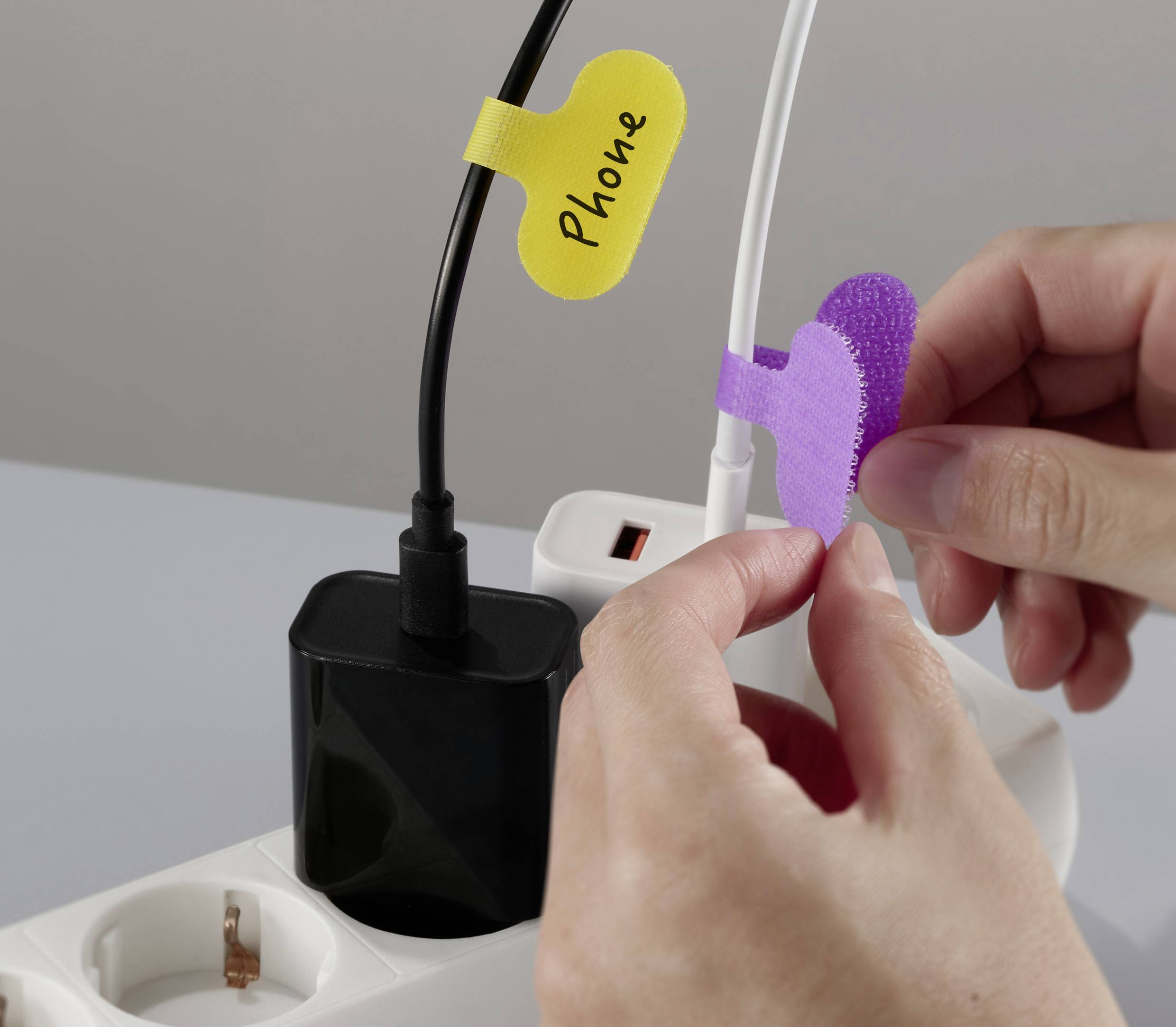 Een persoon ordent kabels met gelabelde tags; een tag op een zwarte kabel heeft met de hand geschreven 'Telefoon', wat kabelmanagement demonstreert.