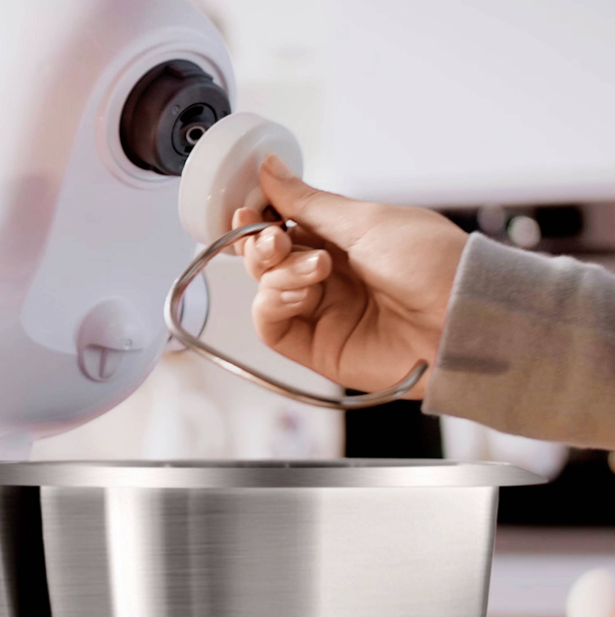 Een persoon bevestigt een deeghaak aan een keukenmachine, deze gereedmakend voor gebruik.