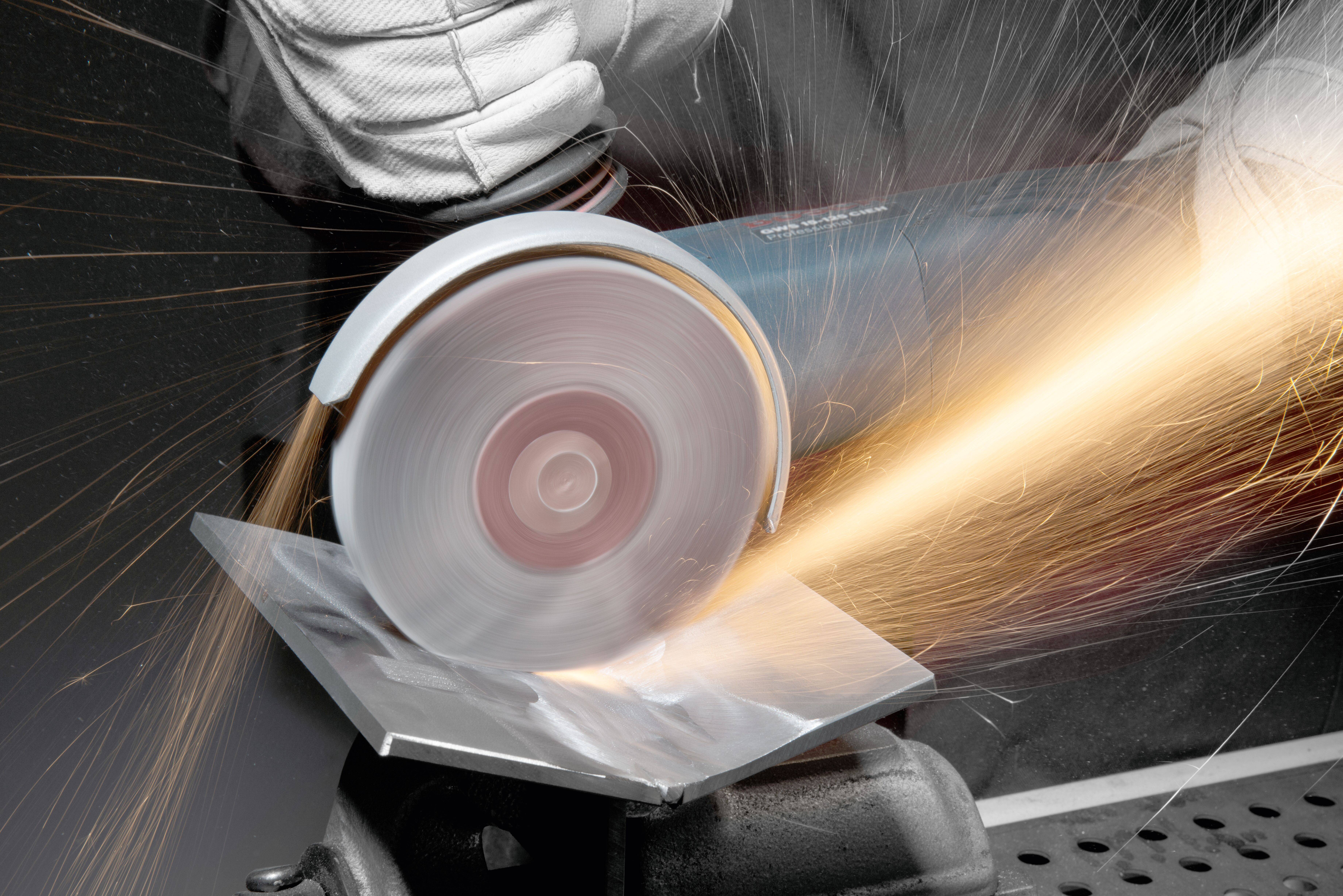 Een persoon die beschermende handschoenen draagt, gebruikt een haakse slijper om een metalen plaat door te snijden, waarbij vonken rond spatten.