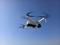 Een witte quadcopter drone zweeft in een heldere blauwe lucht, met zijn rotors wazig door de beweging.