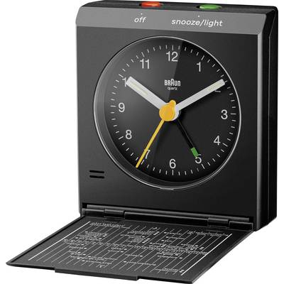 Een zwarte Braun analoge wekker met witte en gele wijzers, waarvan de reiskoffer open staat en een wereldtijdzonelijst aan de binnenkant van het deksel onthult.