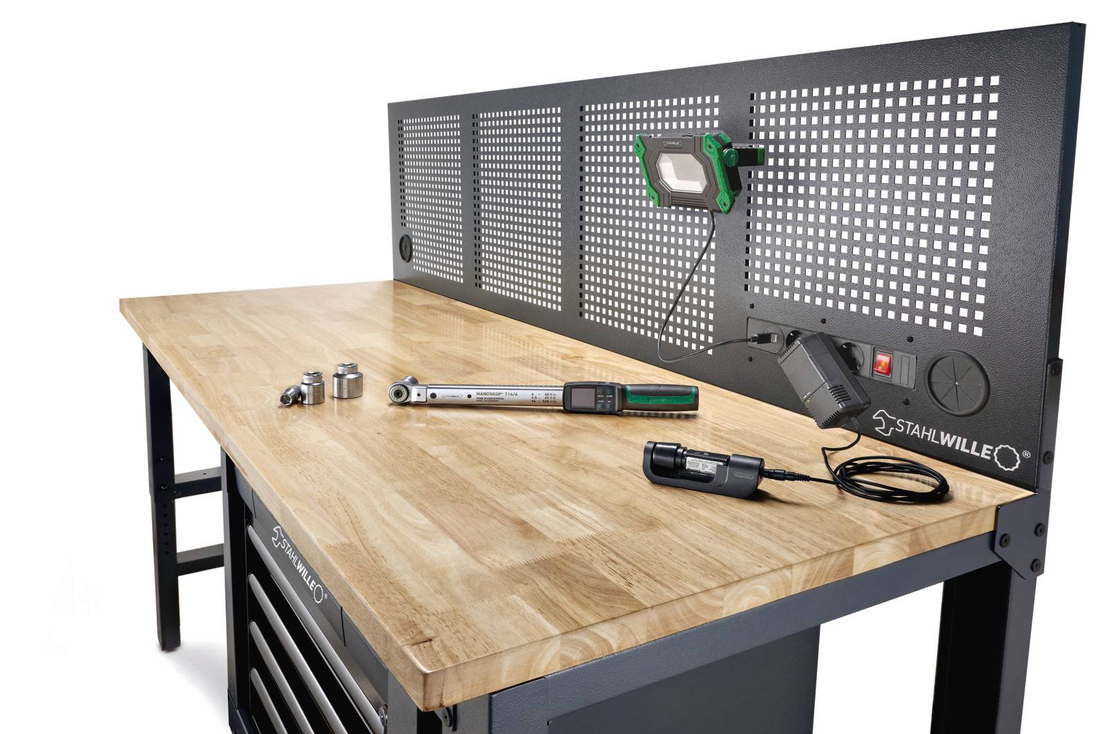 Werkbank met houten blad en zwart metalen gereedschapsbord, waarop een groene lamp staat. Op het werkblad liggen gereedschappen zoals een momentsleutel en dopsleutels.