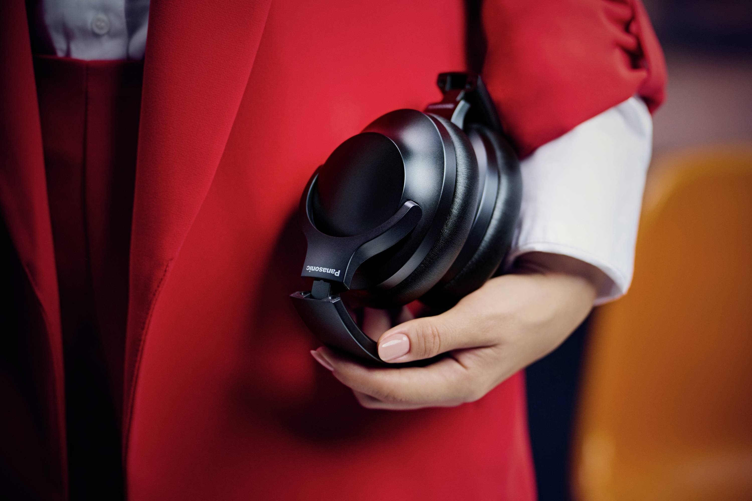Een persoon in een rode jas houdt een paar zwarte koptelefoons vast, wat een mengeling van mode en technologie benadrukt.