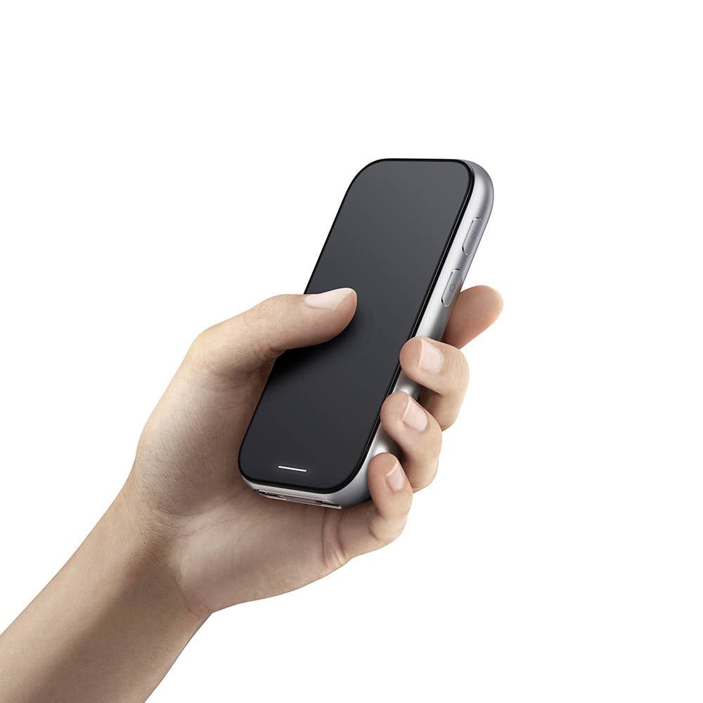 Een hand van een persoon houdt een zwarte smartphone vast, met een effen zwart scherm, tegen een witte achtergrond.