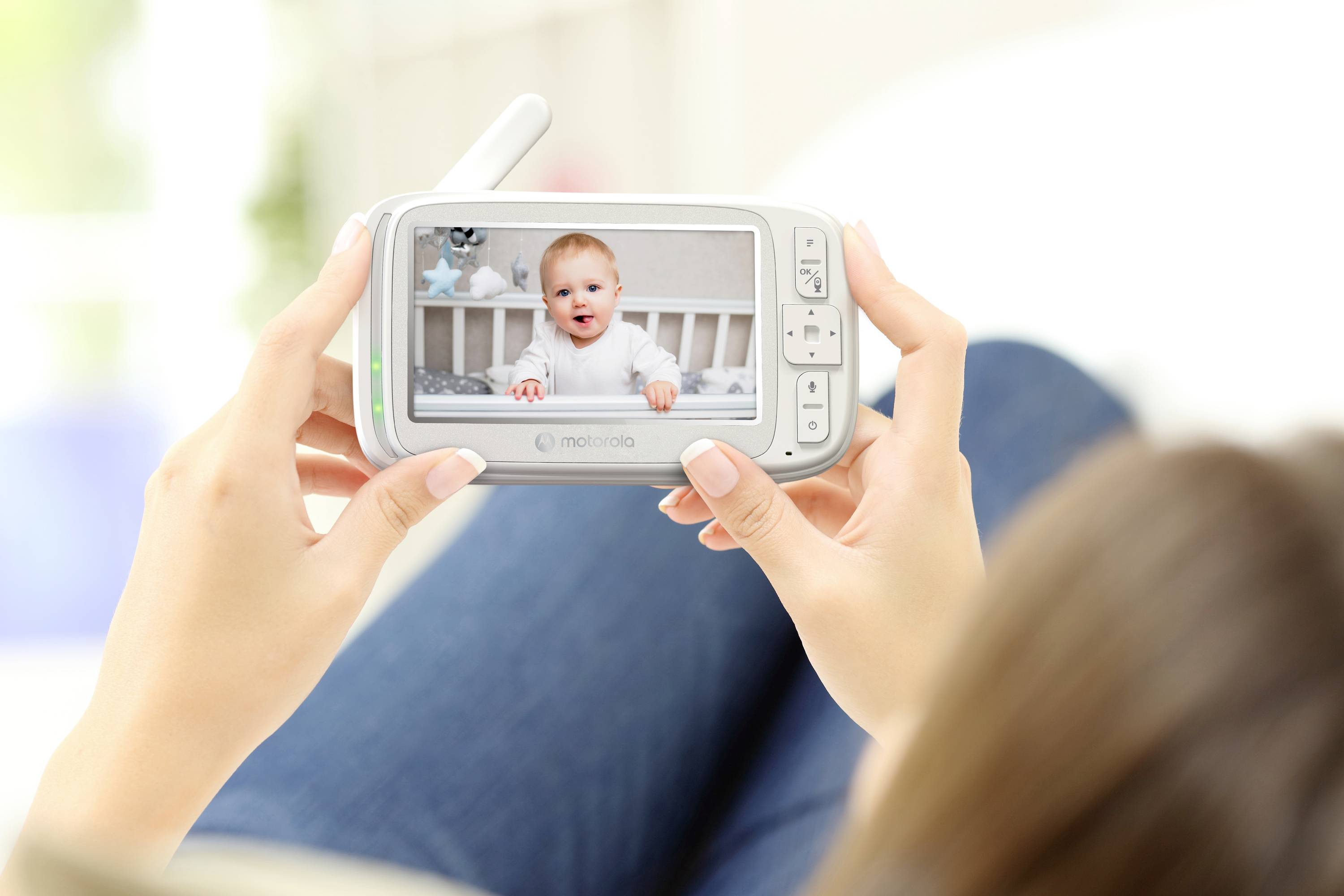 'Een persoon houdt een babyfoon vast waarop een lachende baby in een wieg te zien is, wat op afstand meekijken met een baby illustreert.'