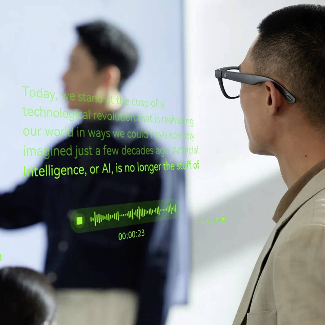 Een man staat naast een transparant scherm waarop tekst over technologie en AI wordt weergegeven, met op de achtergrond een andere persoon die naar een bord wijst.