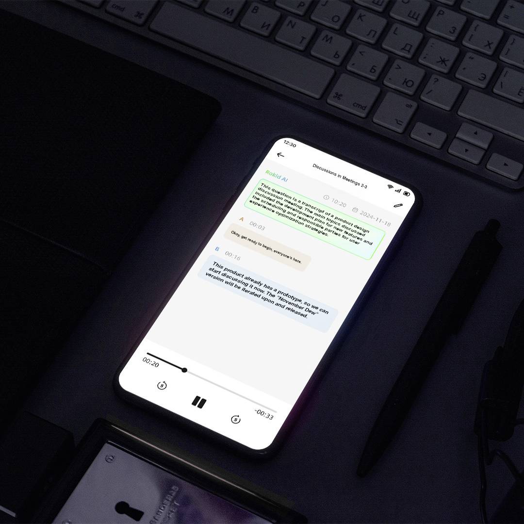 Een smartphone op een bureau toont een chatgesprek in een app tussen twee gebruikers, waarbij 'Design QA' en 'Ryan Gosling films' worden vermeld. Een afspeelknop is zichtbaar.