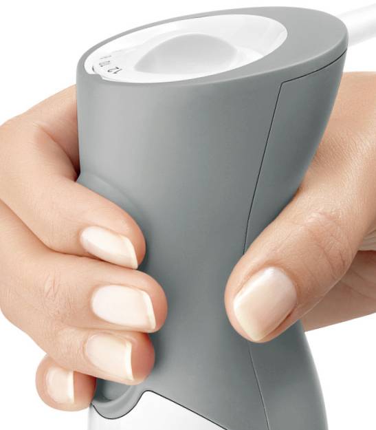 Een hand grijpt een grijze ergonomische handgreep van een apparaat, waarbij de bovenaanzicht van de handgreep wordt getoond met een witte knop erop.