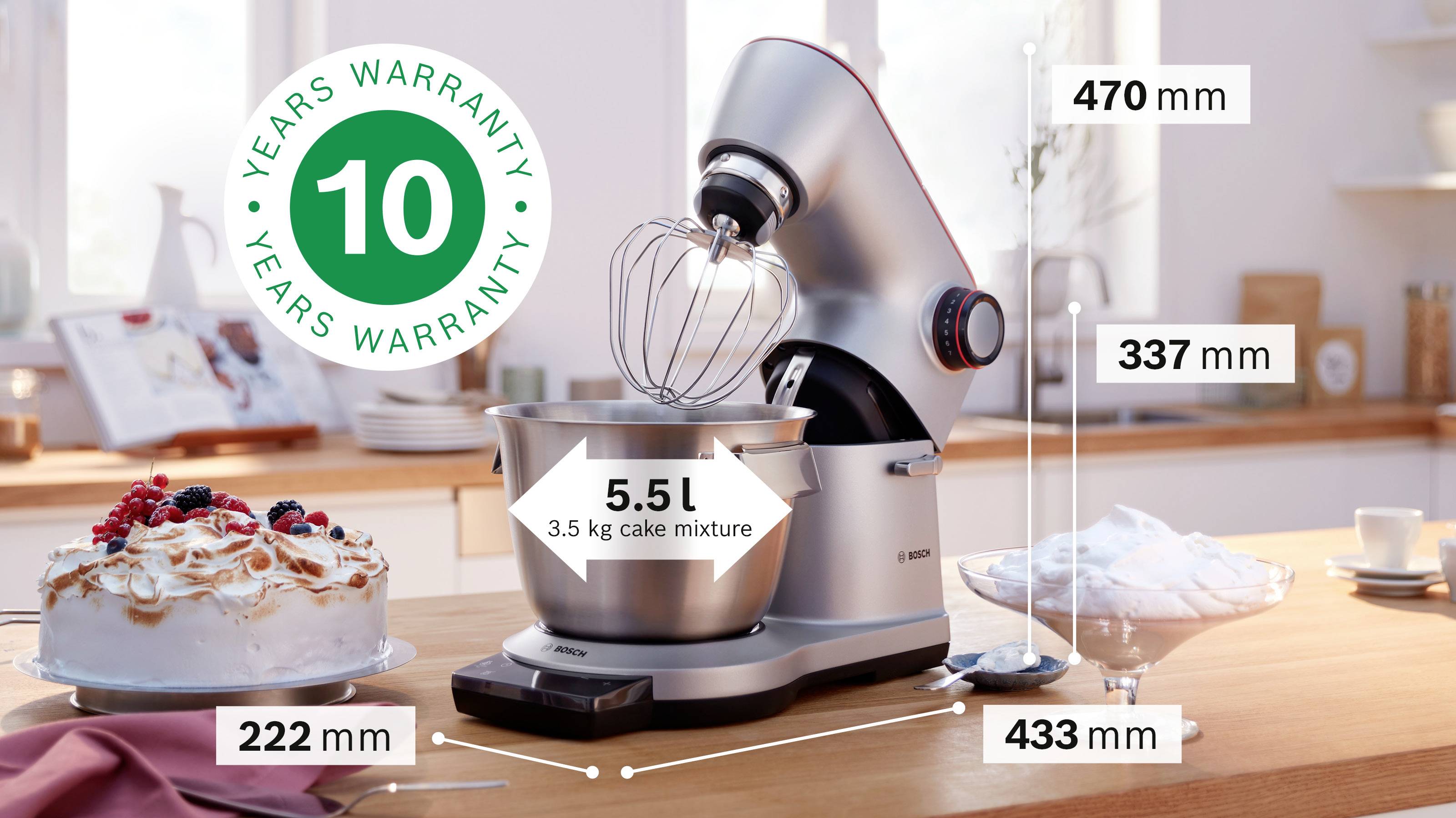 Een zilveren keukenmixer met een garde, met een kom voorzien van het label '5,5 L, 3,5 kg cakebeslag'. Afmetingen: 470 mm hoogte, 337 mm diepte, 433 mm breedte, 222 mm komdiameter. '10 jaar garantie' badge. Cake op het aanrecht.