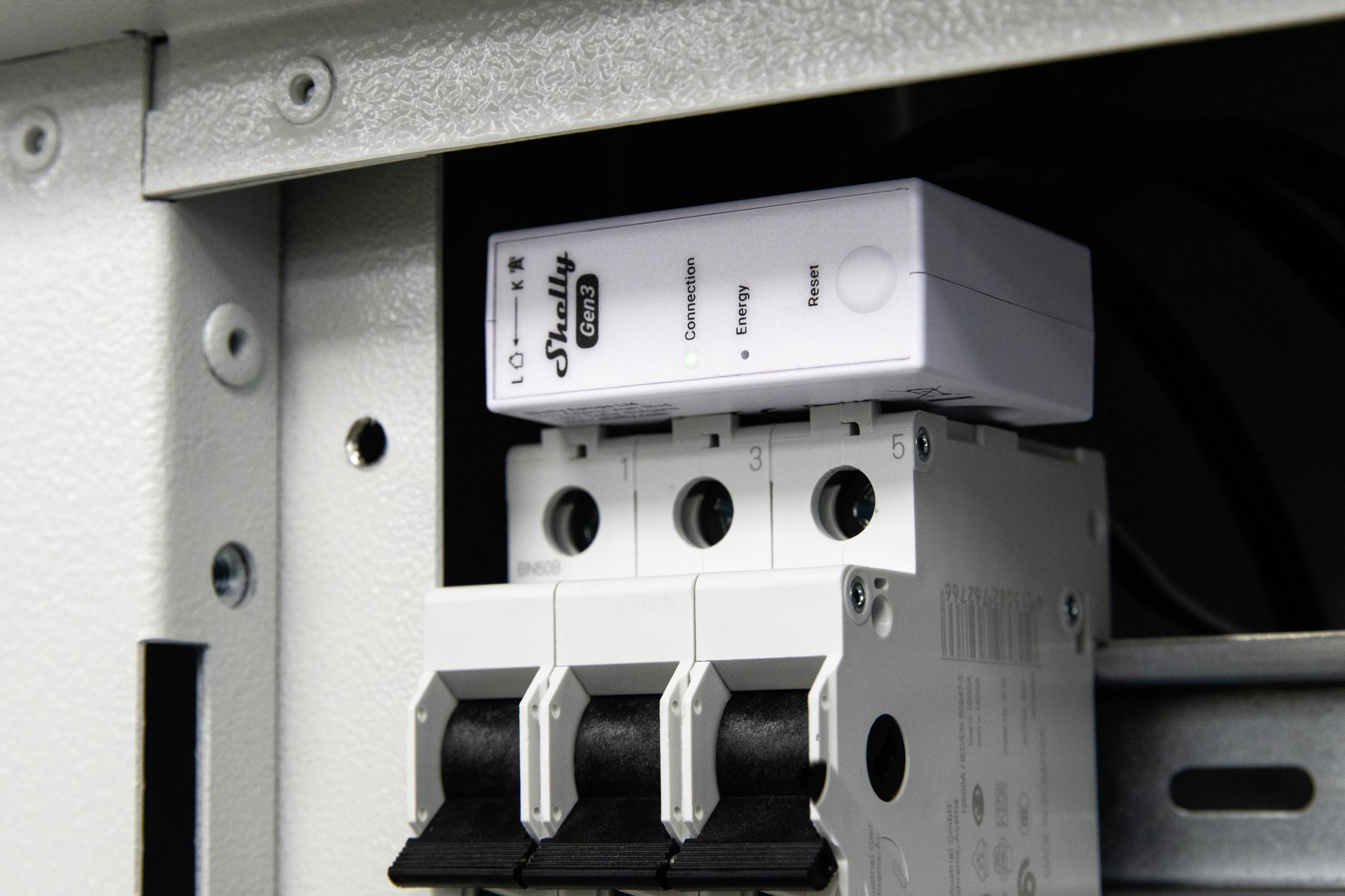 Een close-up van een elektriciteitspaneel waarop een Shelly energiemonitoringsapparaat is geplaatst bovenop installatieautomaten in een metalen behuizing.