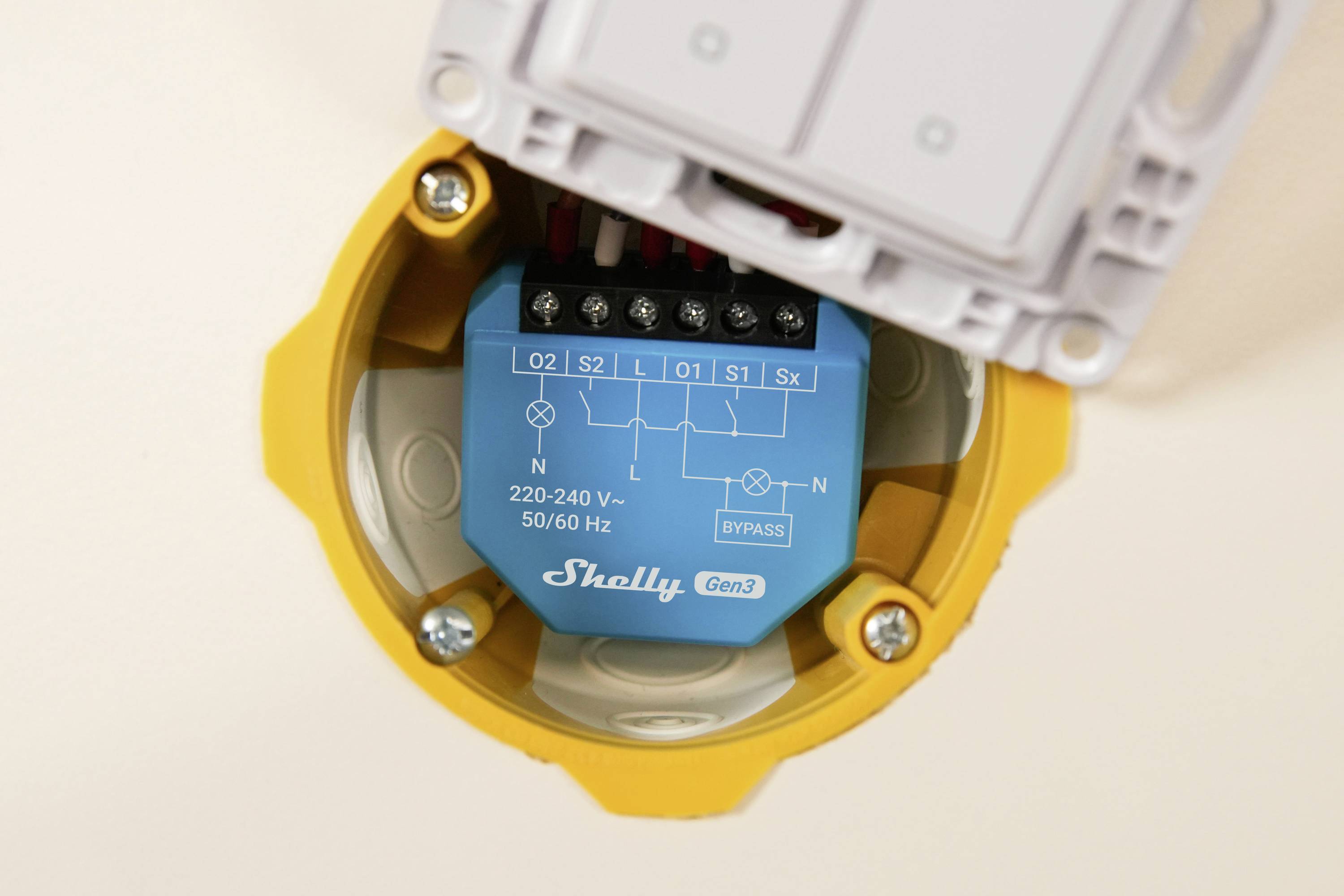 Een elektrisch apparaat geïnstalleerd in een rond geel behuizing. Het toont aansluitingen en schematische details voor 220-240V, 50/60Hz voeding.
