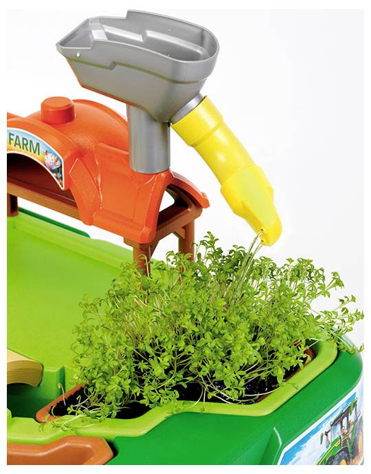 Een speelgoed boerderijset met een plastic gieter die water giet op kleine groene plantjes. Het etiket vermeldt 'BOERDERIJ' boven de scène.