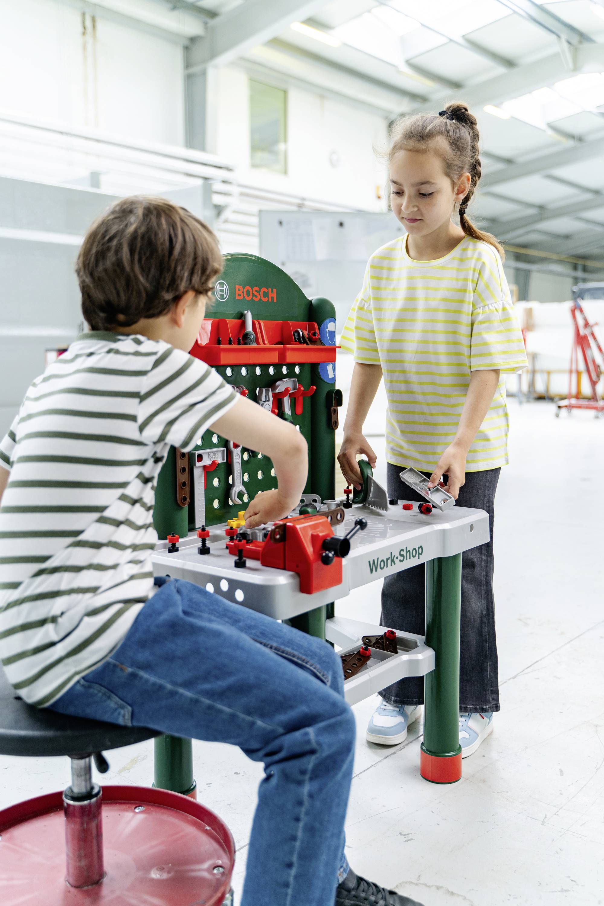 Twee kinderen spelen met een speelgoed werkbank en wijden zich aan creatieve constructieactiviteiten in een lichte, ruime kamer.