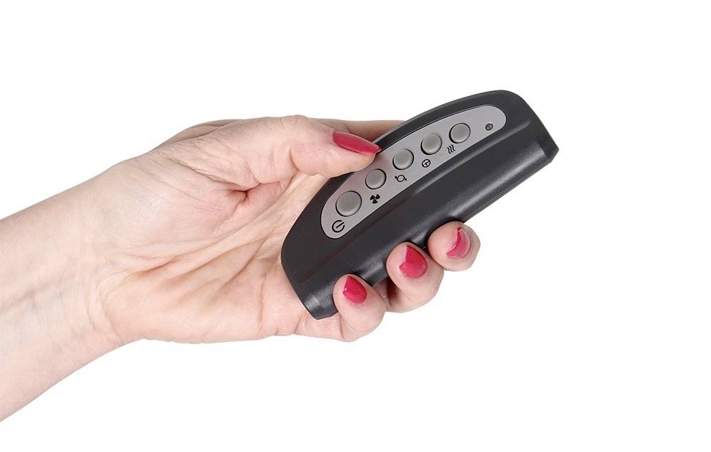 Een hand met rode nagels houdt een zwarte afstandsbediening vast, met verschillende knoppen, tegen een witte achtergrond.