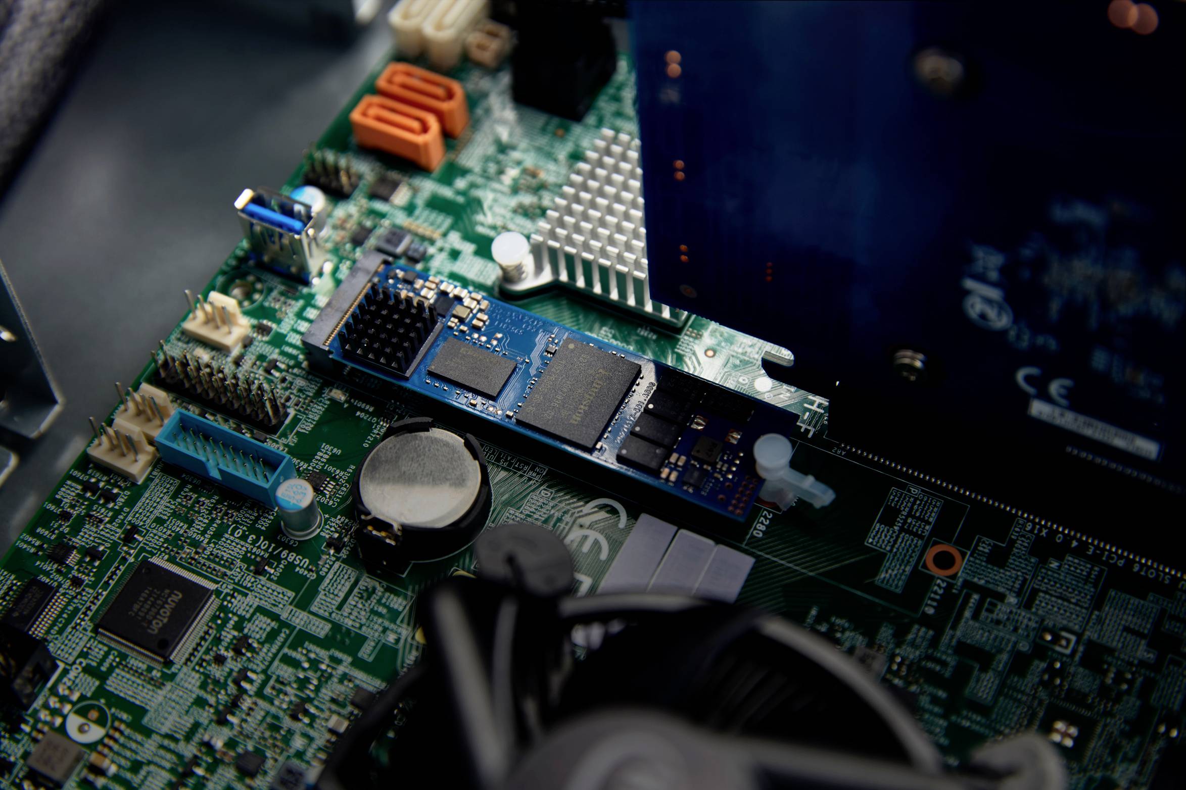 Een close-up van een computermoederbord, met verschillende componenten zoals een blauwe uitbreidingskaart, condensatoren en aansluitingen, in een behuizing.